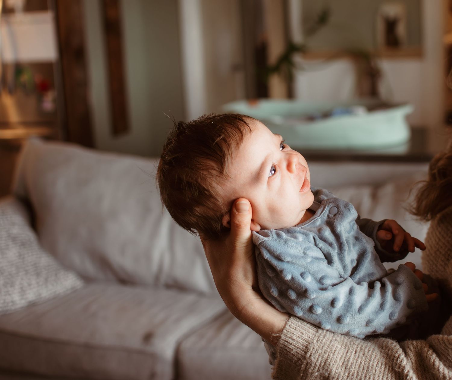 A sleeping infant wearing a light blue outfit lies peacefully on a cozy white bedding surface.