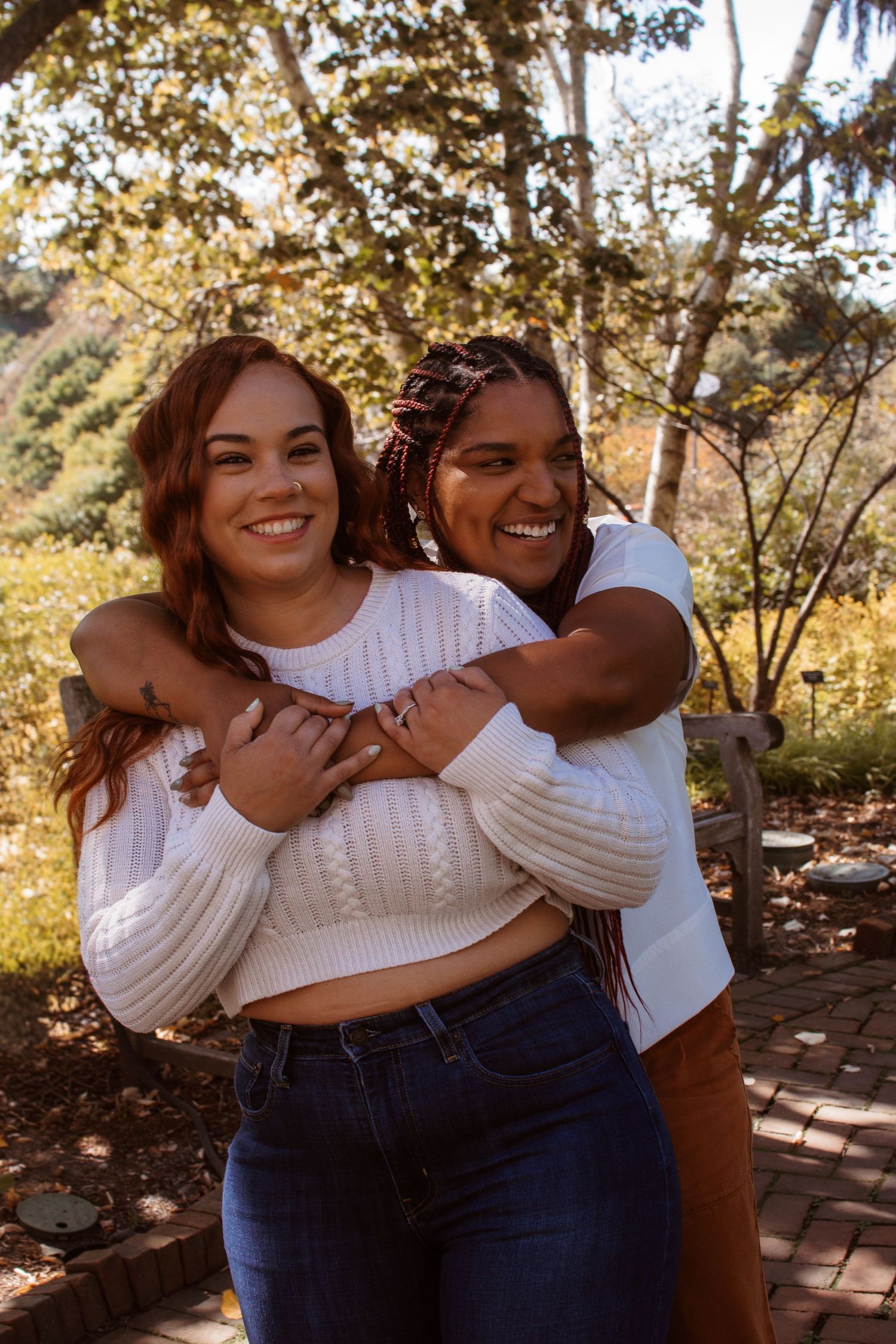 A couple in casual white tops share joyful embraces and laughter during an outdoor photoshoot on a brick patio.