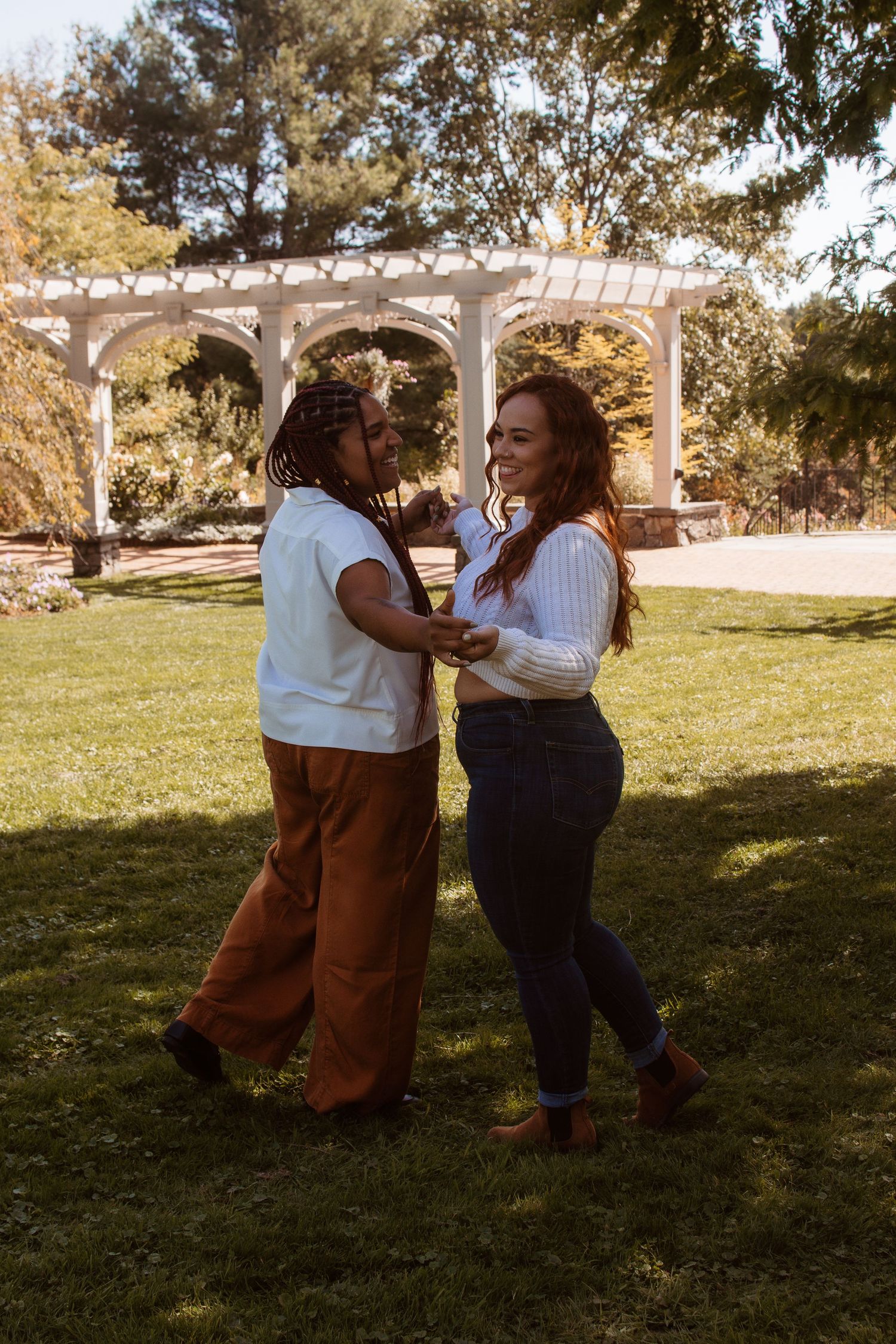 Two people share a joyful moment dancing together on a grassy lawn under trees on a sunny day.