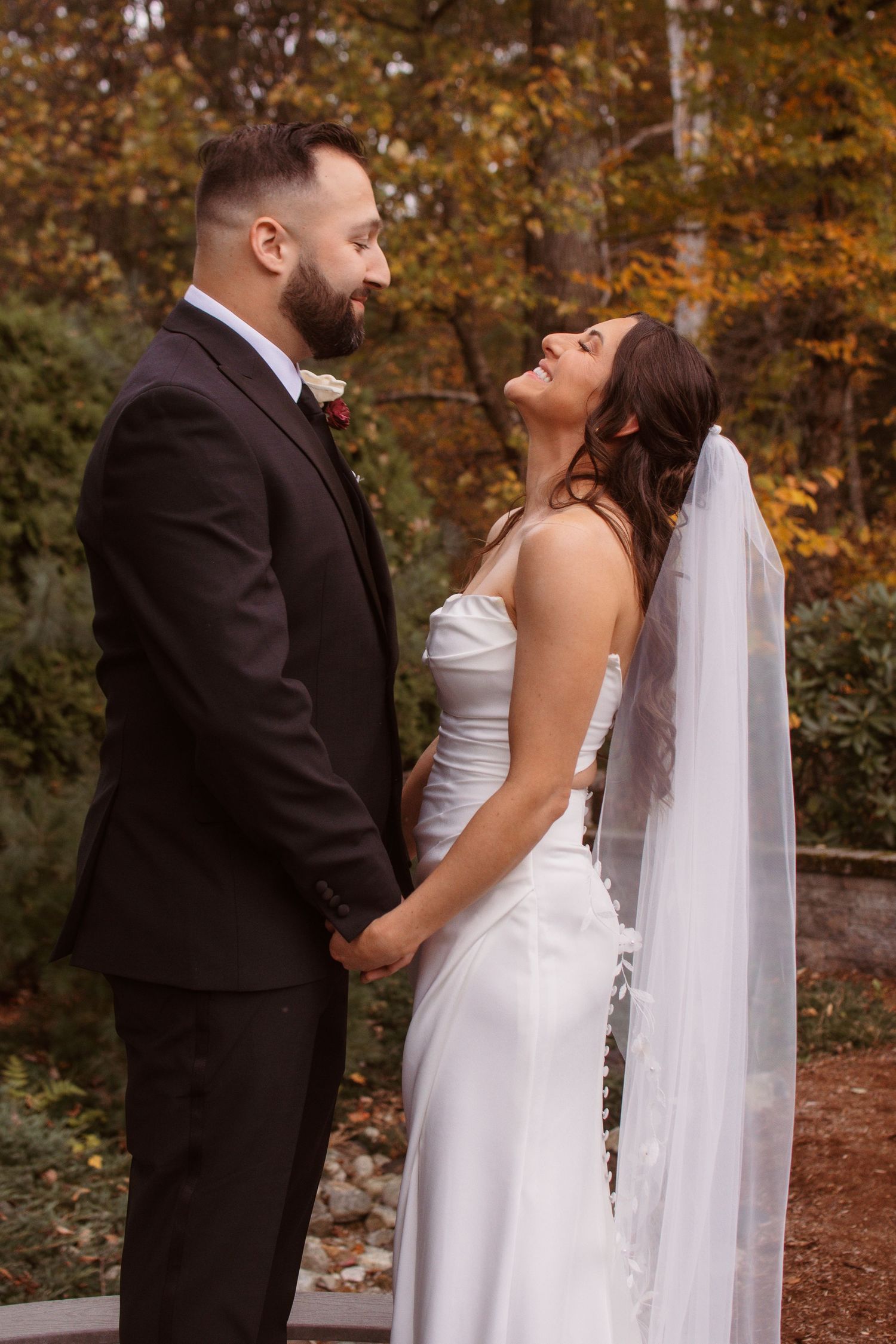 Newlywed couple shares romantic moments in autumn forest setting with golden foliage in background.