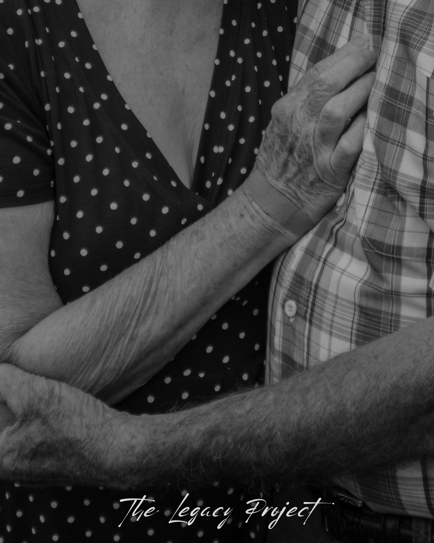Black and white photograph showing hands clasped together against a polka dot and plaid patterned background.