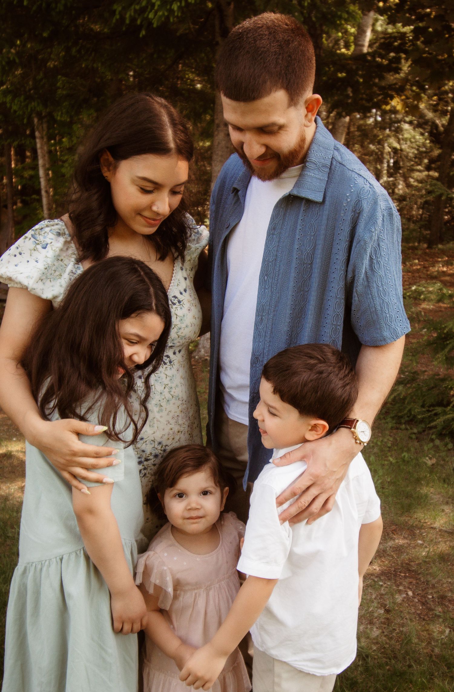 A family shares a tender moment together outdoors, dressed in coordinating white and blue casual attire.