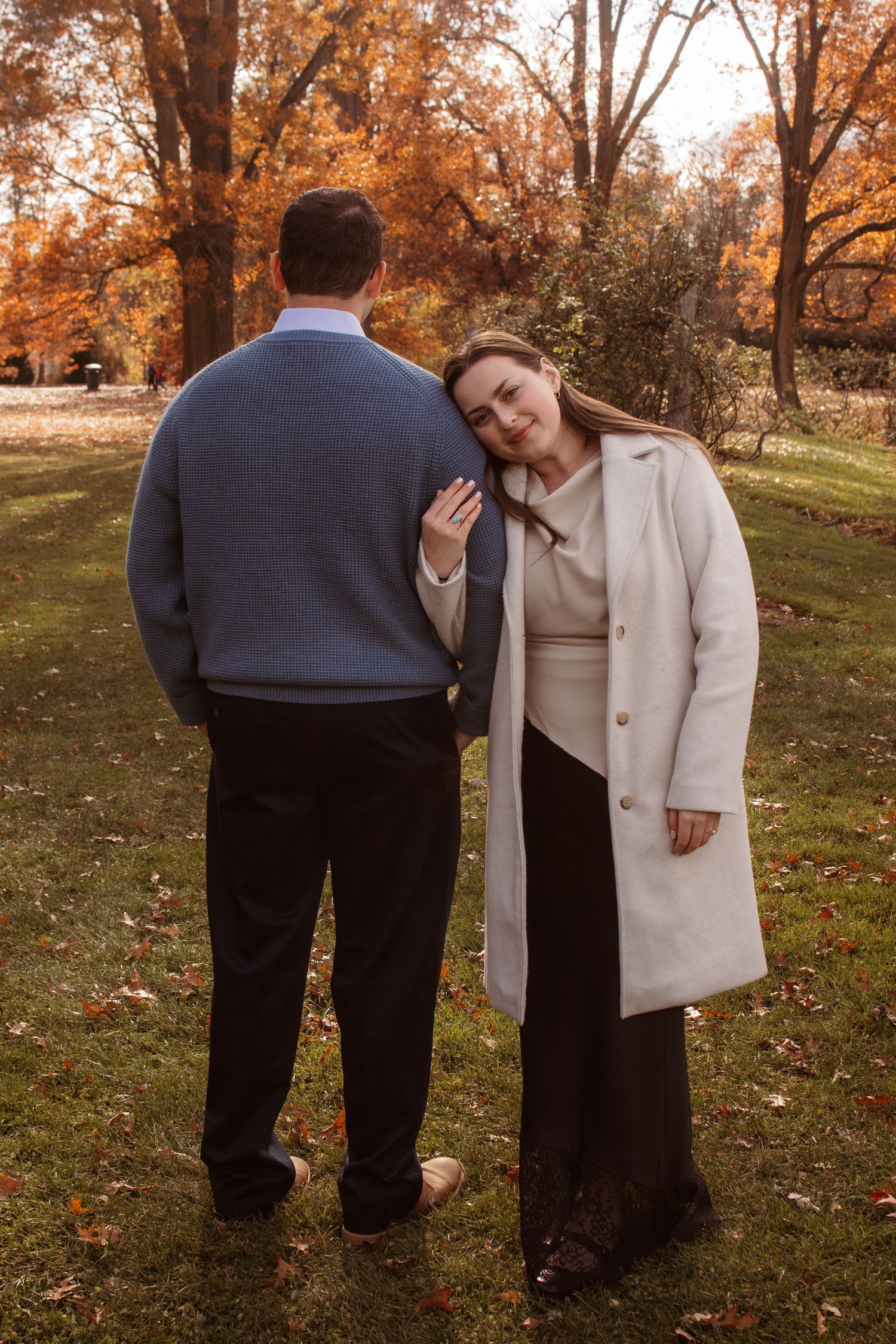 A couple in autumn attire sharing a tender moment among fall foliage in a park setting.