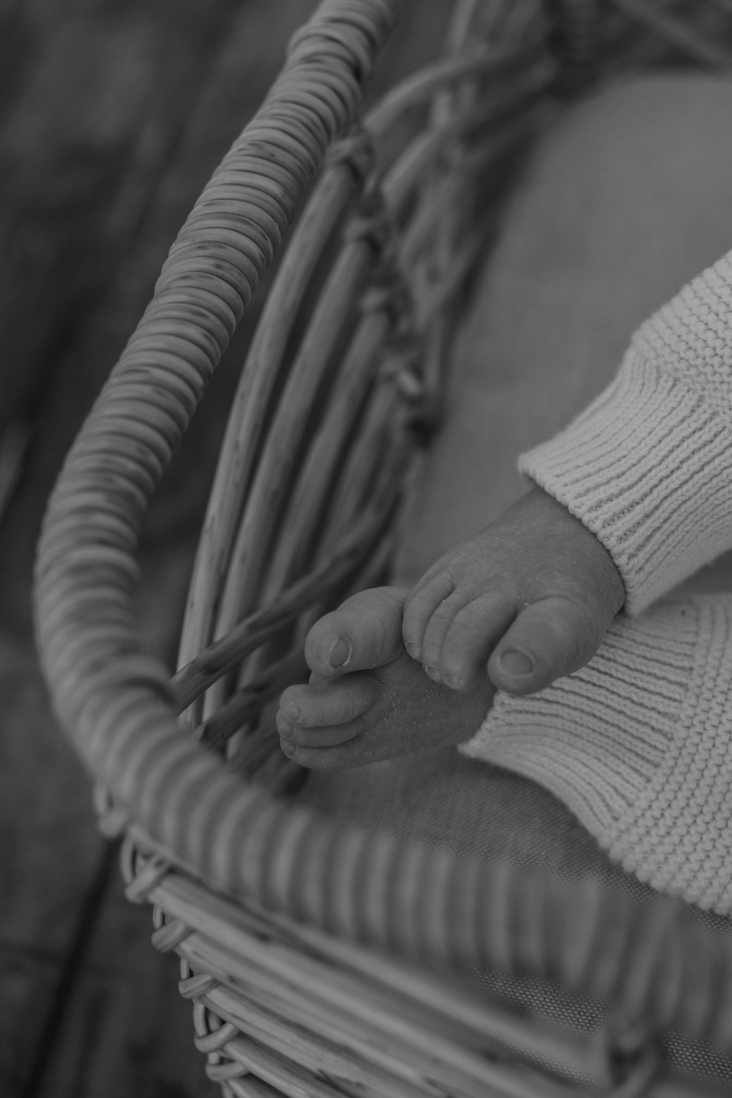 Black and white close-up of tiny newborn baby feet resting in a wicker bassinet with soft fabric lining.