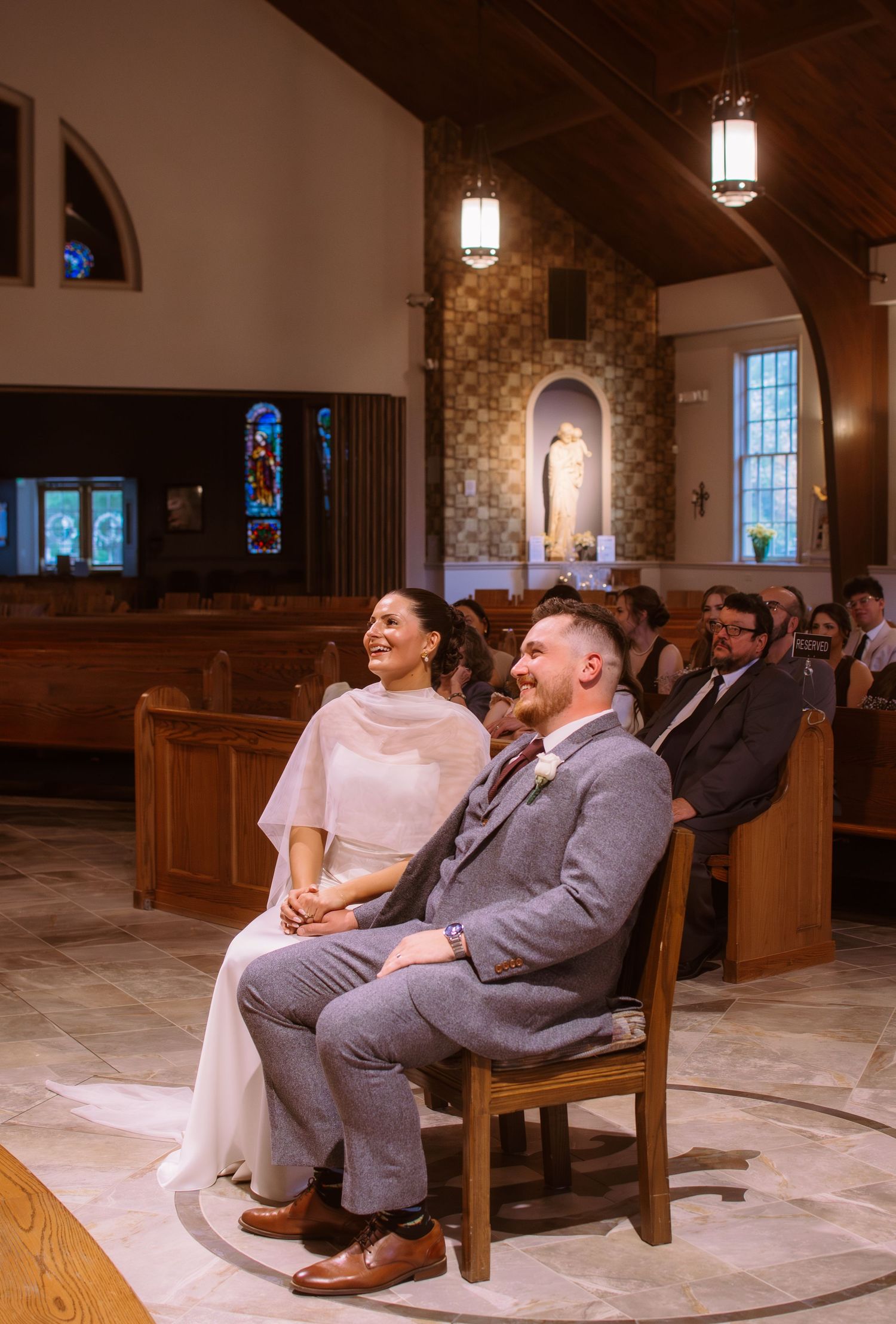 A bride and groom sit together smiling during their wedding ceremony inside a beautiful Catholic church.