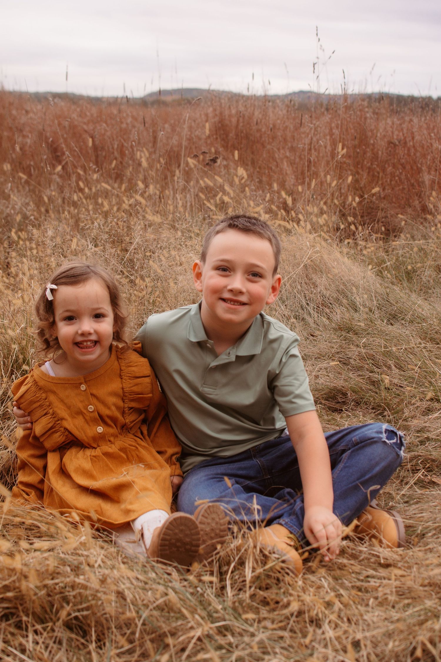 Two young children laughing and playing together while sitting in a golden autumn field of tall grass.