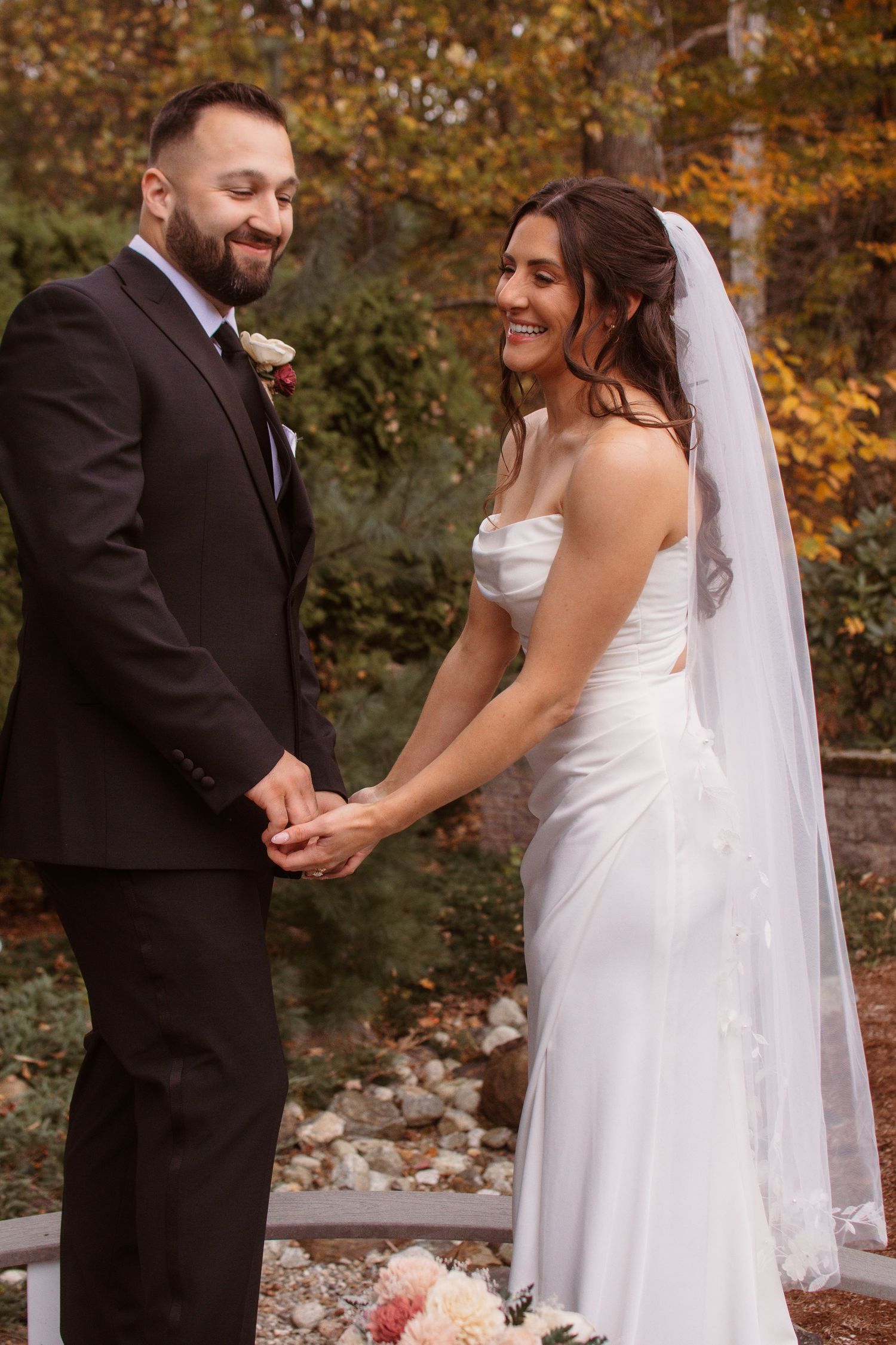A bride and groom share joyful moments during their autumn wedding photoshoot with golden foliage in the background.
