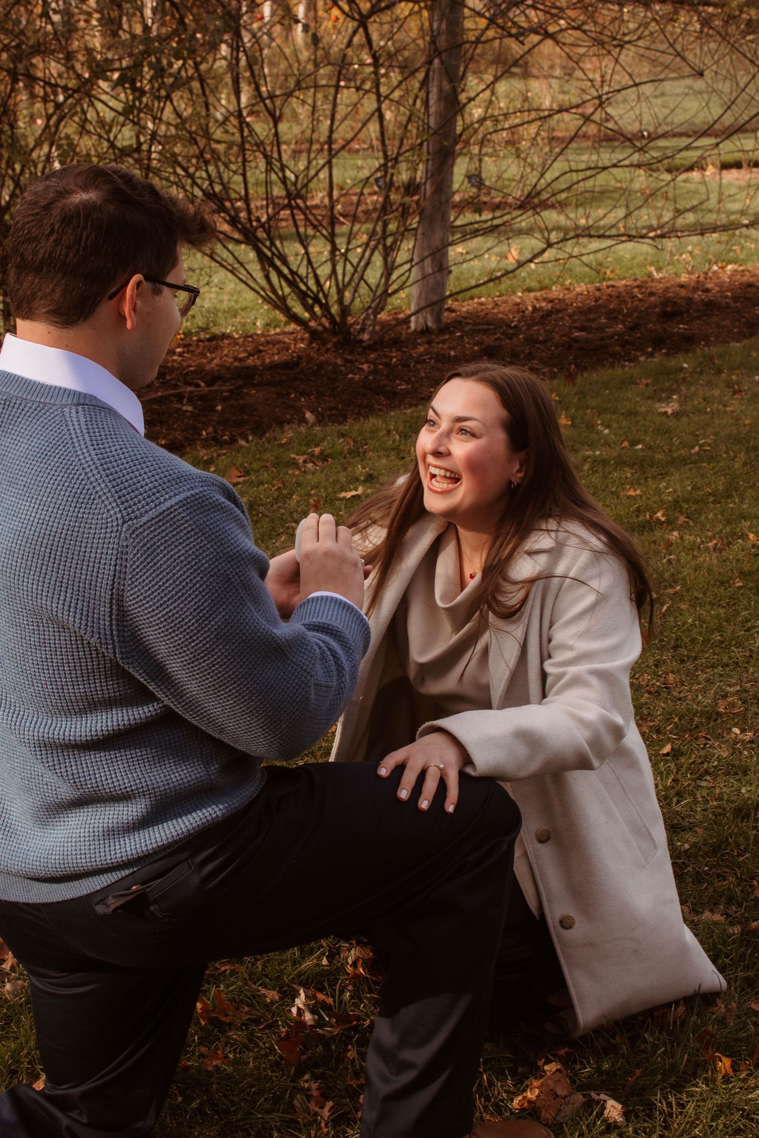 Two people engage in a playful mock fight scene among fall foliage in a park setting.