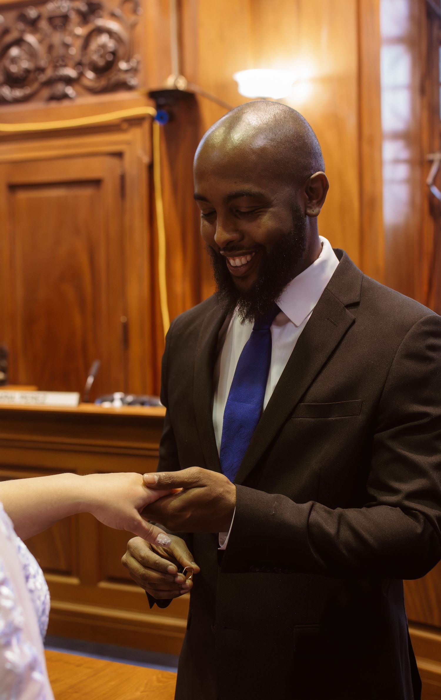 Professional in a dark suit and blue tie smiles warmly while engaging in conversation in an elegant wood-paneled room.