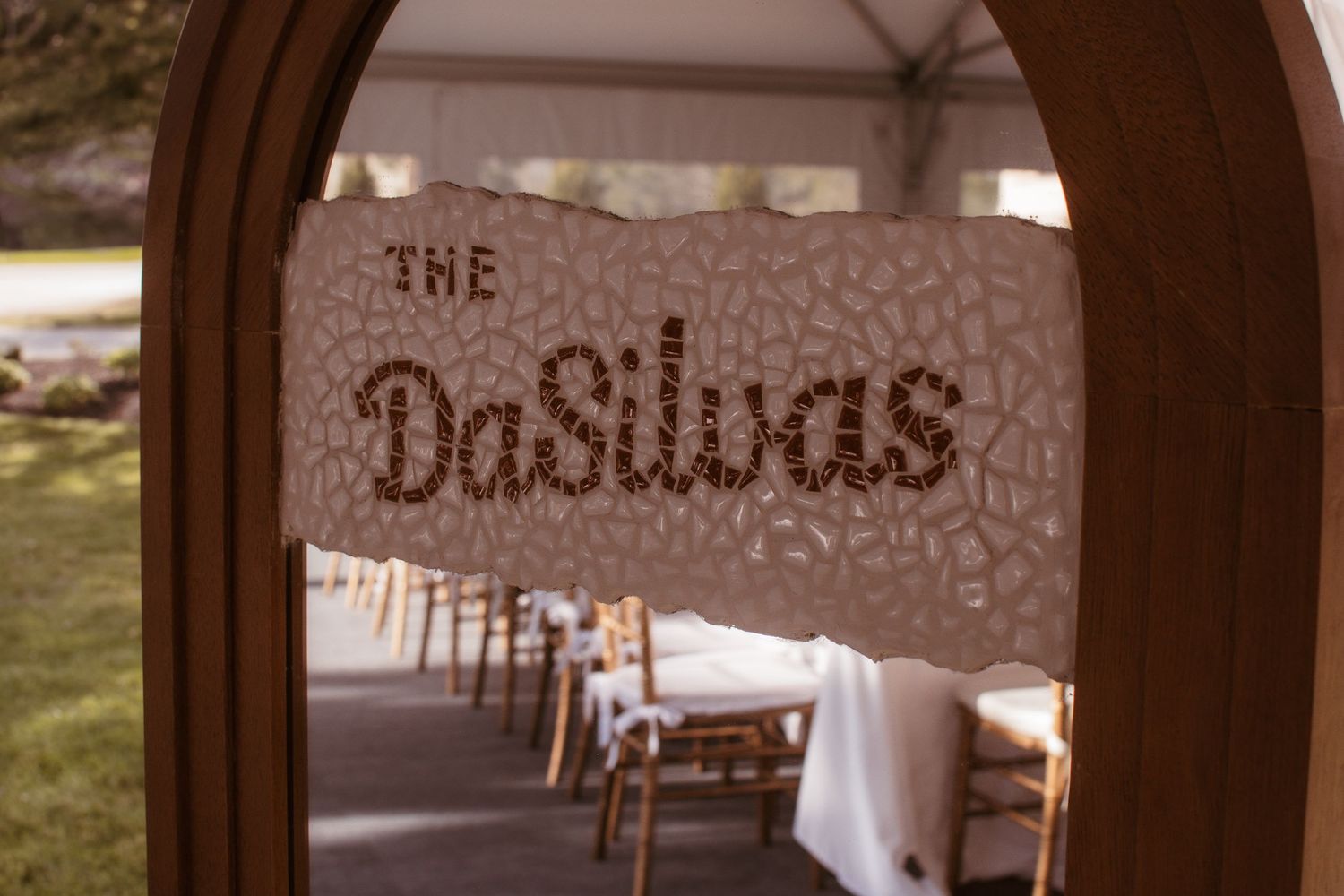 Elegant wedding sign reading The DaSilvas displayed in a decorative wooden arch at a tented reception.