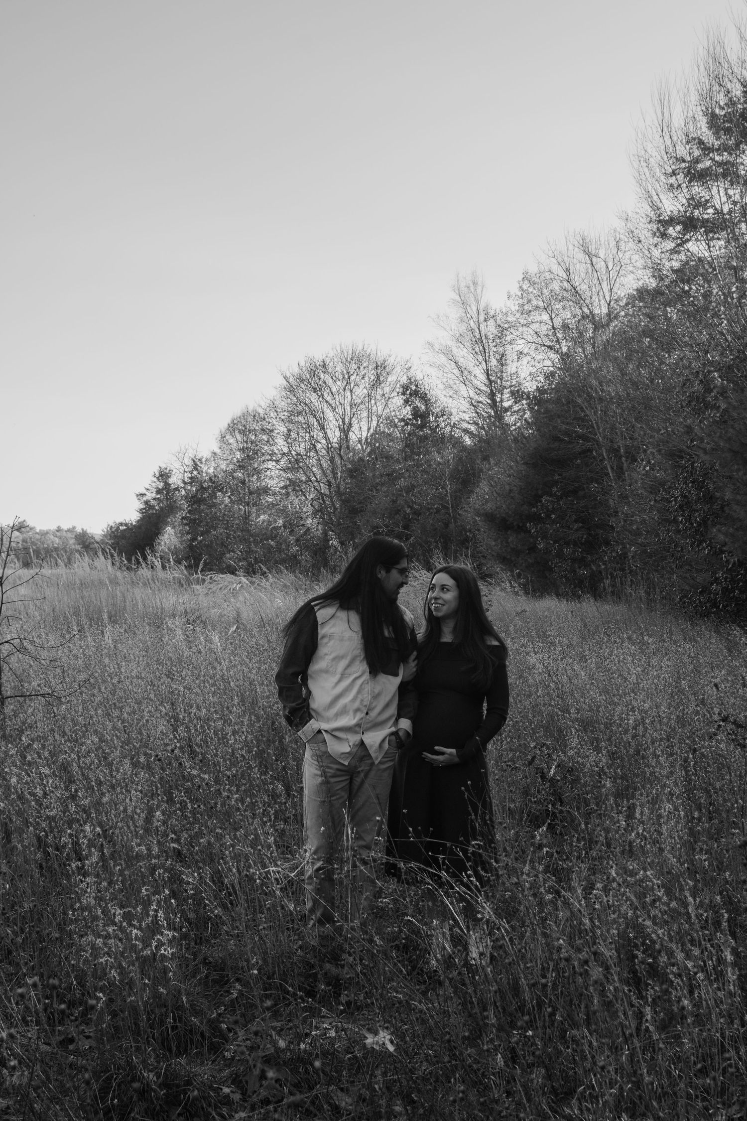 Black and white photo series shows two figures embracing in a tall grass field with trees in background.