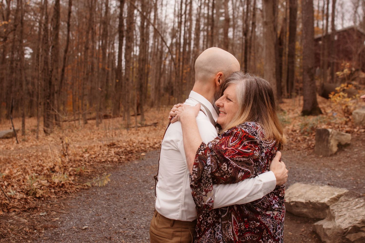A couple walks hand in hand down a wooded trail during autumn with fallen leaves covering the ground.