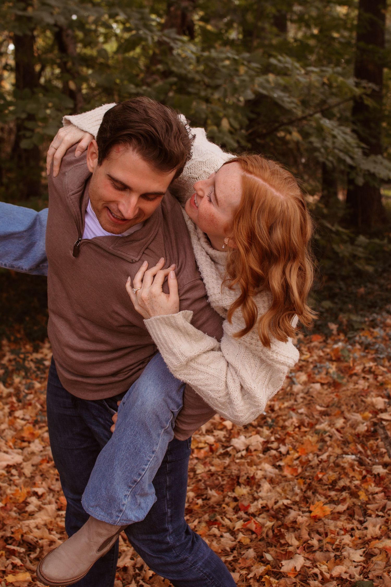 A couple shares a playful moment while sitting on autumn leaves in a romantic outdoor photoshoot.