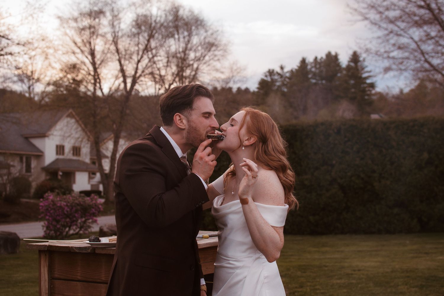 Bride and groom sharing wedding cake at outdoor reception during golden hour.