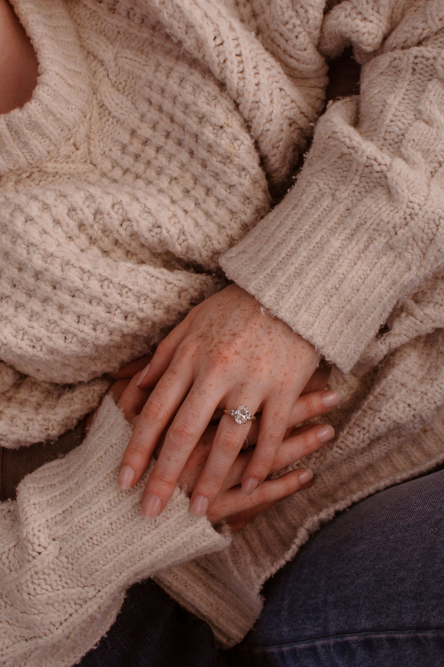 Close-up view of hands wearing an engagement ring with a cozy cream knit sweater.