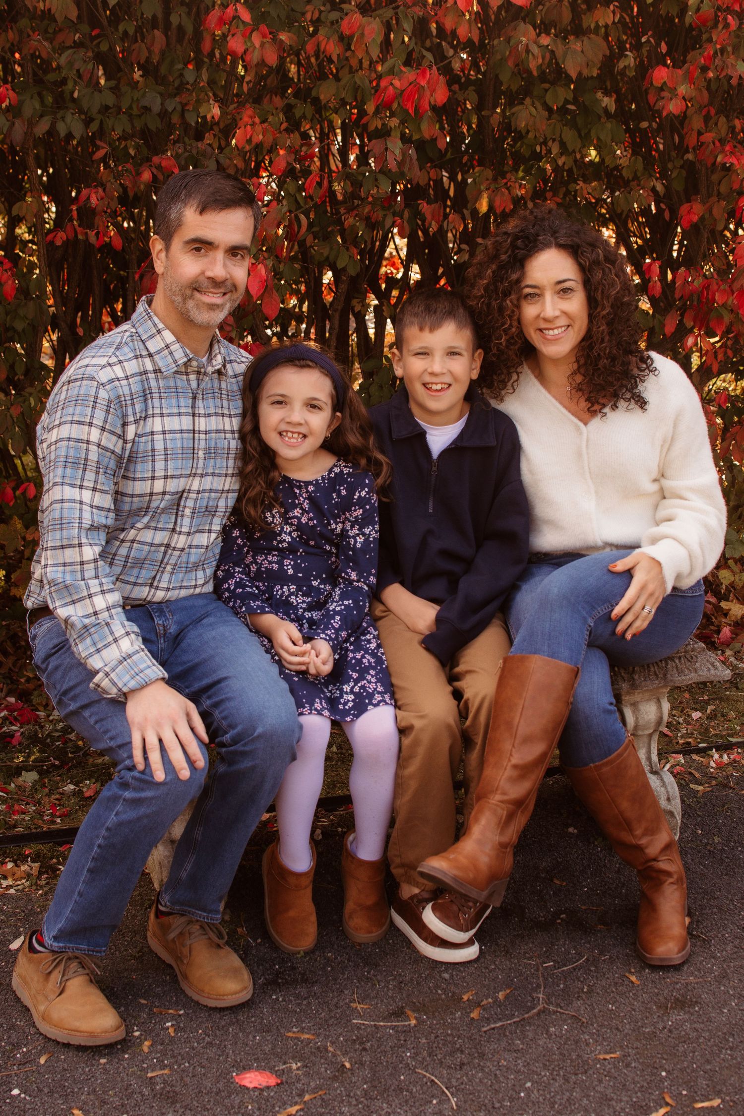 A group sits together on a stone ledge against a backdrop of vibrant red autumn foliage.