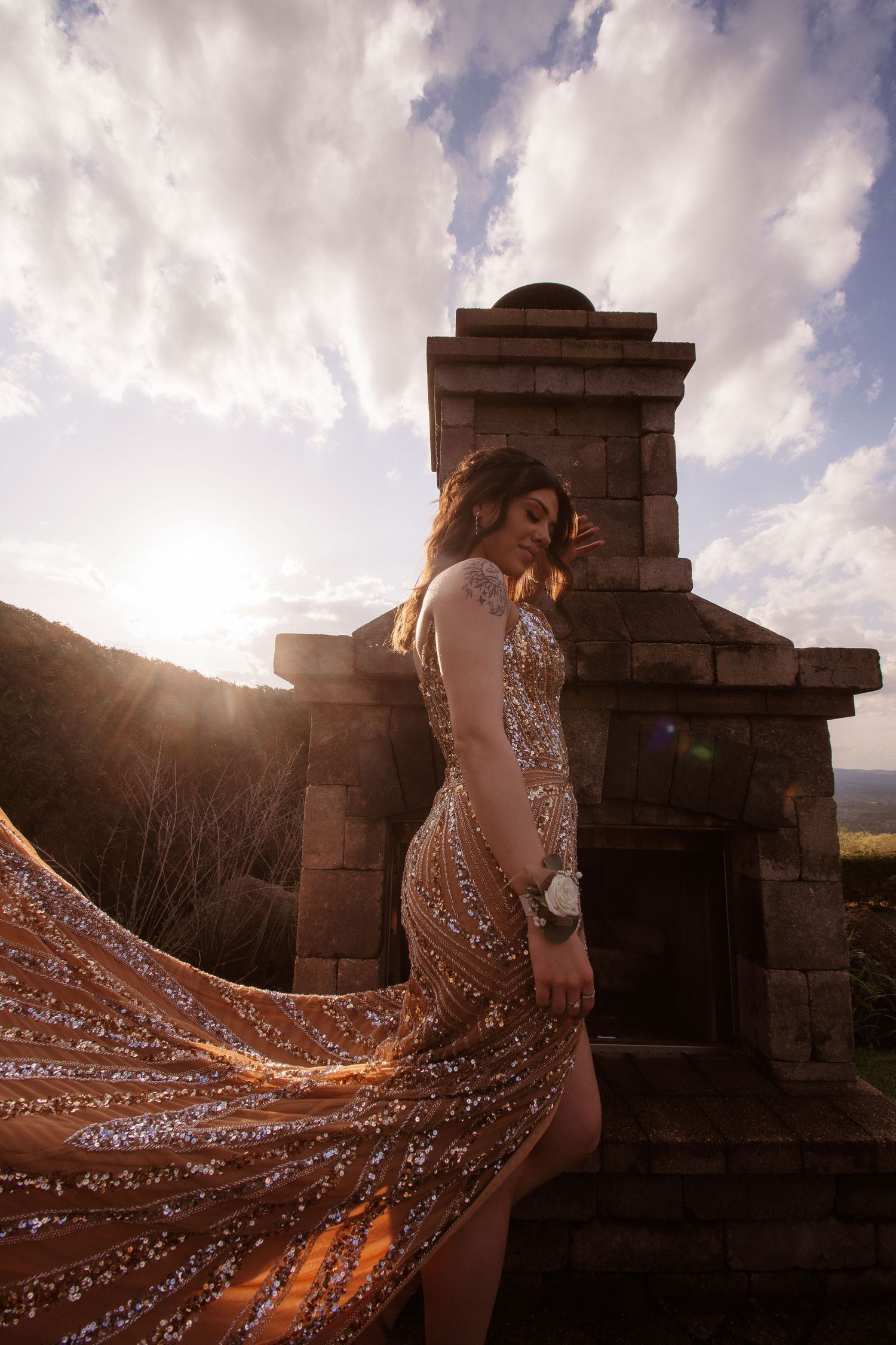 A sparkling gown with a dramatic flowing train catches the golden sunlight against an ancient stone structure background.
