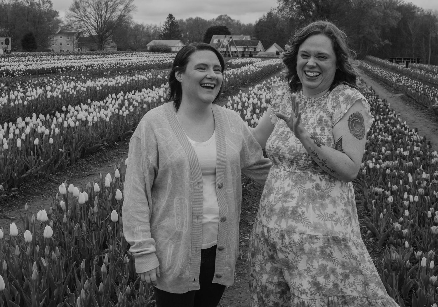 Two women laughing joyfully in a tulip field, black and white photo taken outdoors near a farmhouse.