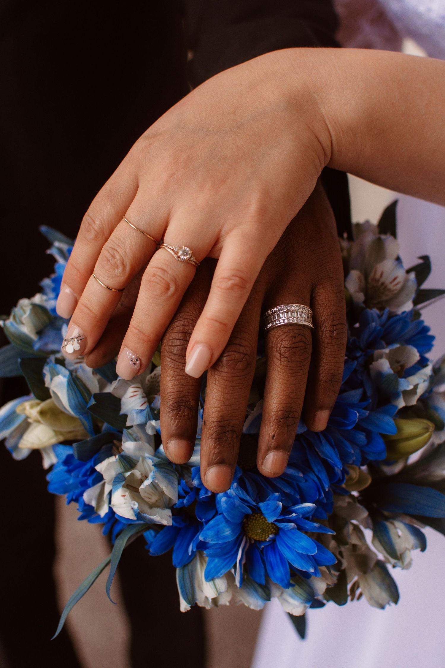 Close-up sequence of hands with engagement rings touching blue and white floral bouquet decorations.