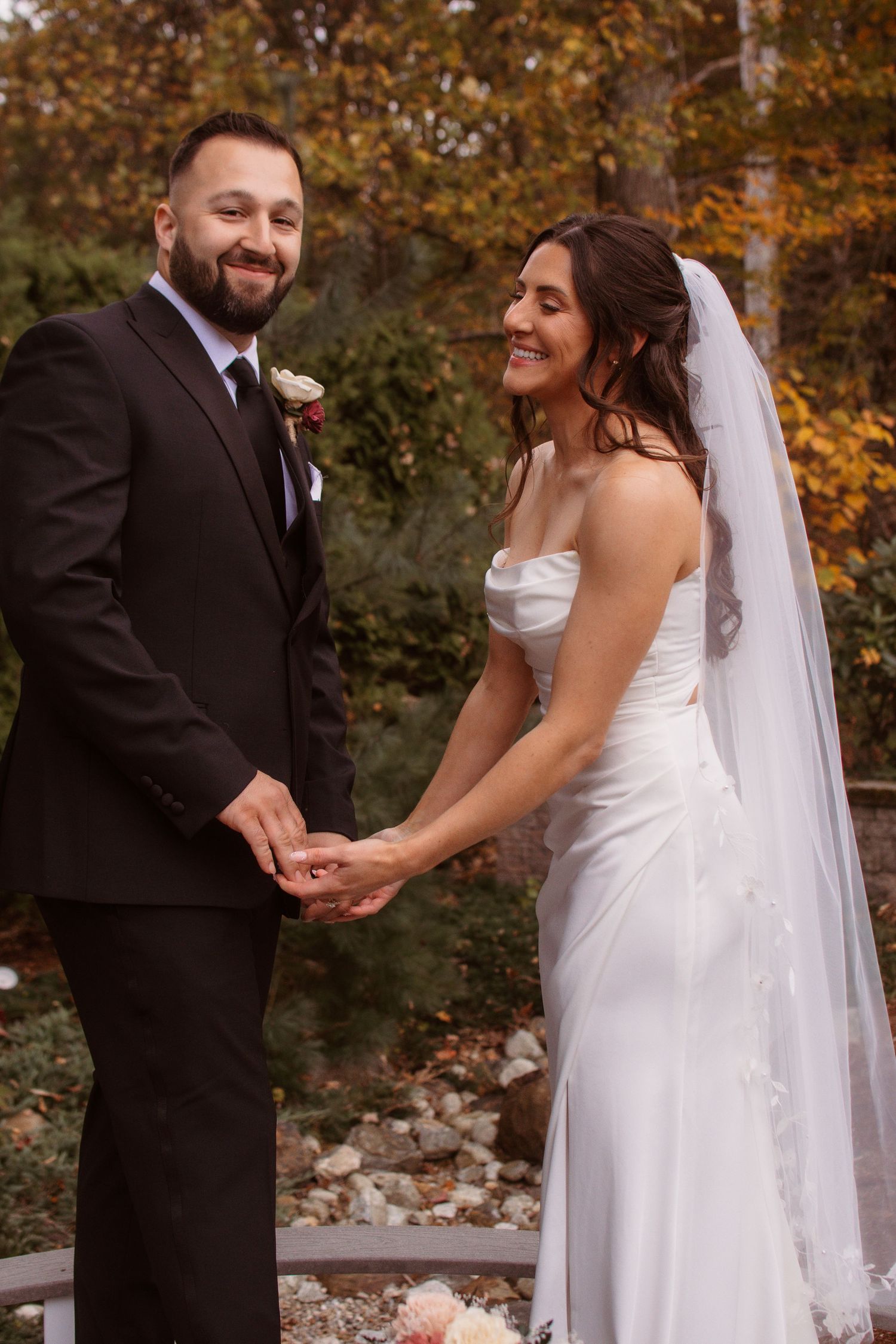A couple shares a joyful moment during their outdoor autumn wedding photoshoot with fall foliage in the background.