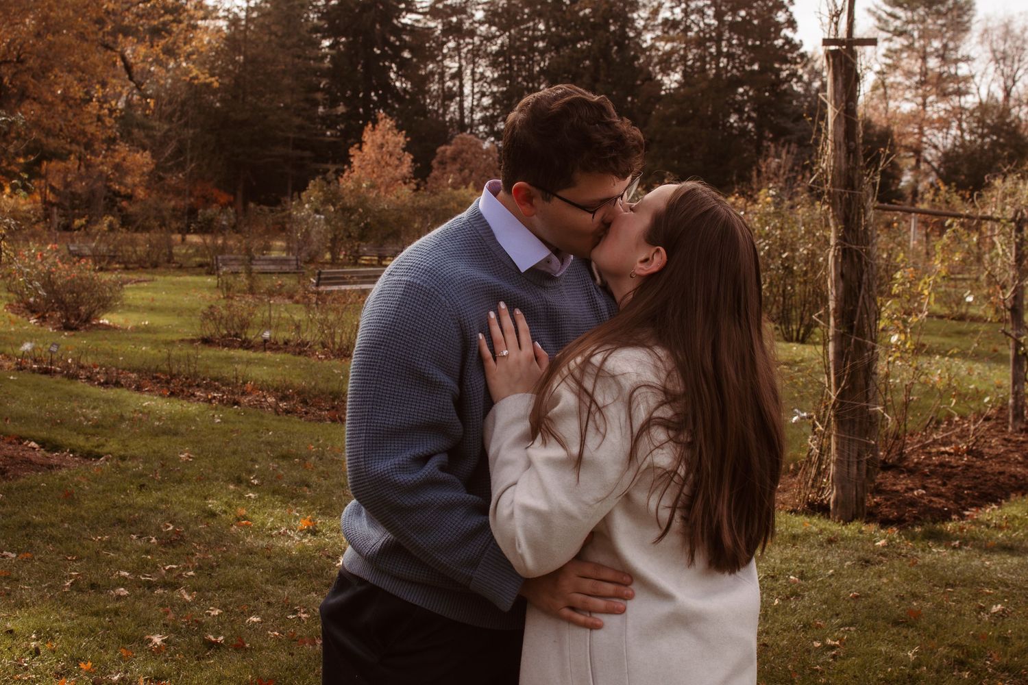A couple shares romantic moments in a scenic autumn garden setting during a golden hour photoshoot.