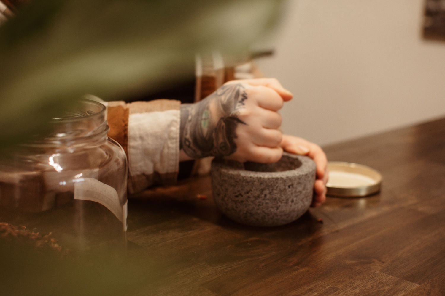 Person grinding ingredients in a stone mortar using a mortar and pestle on a wooden surface in warm lighting.