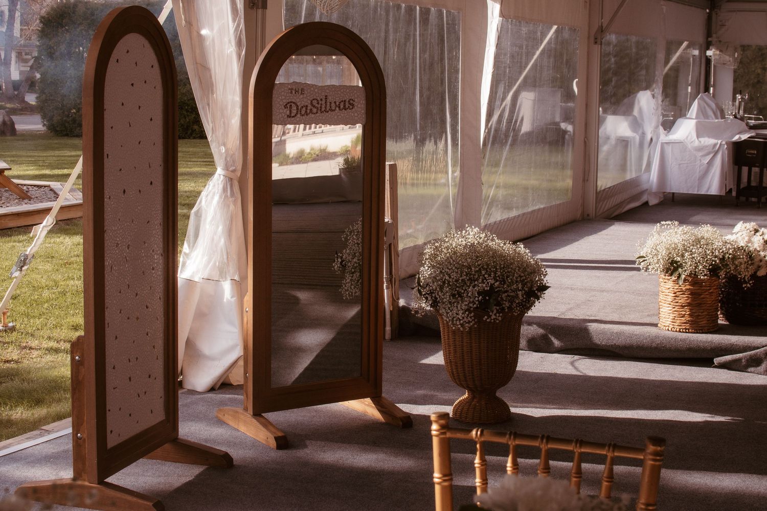 Elegant wooden arched mirror and floral arrangements decorate a wedding venue tent with white draping.