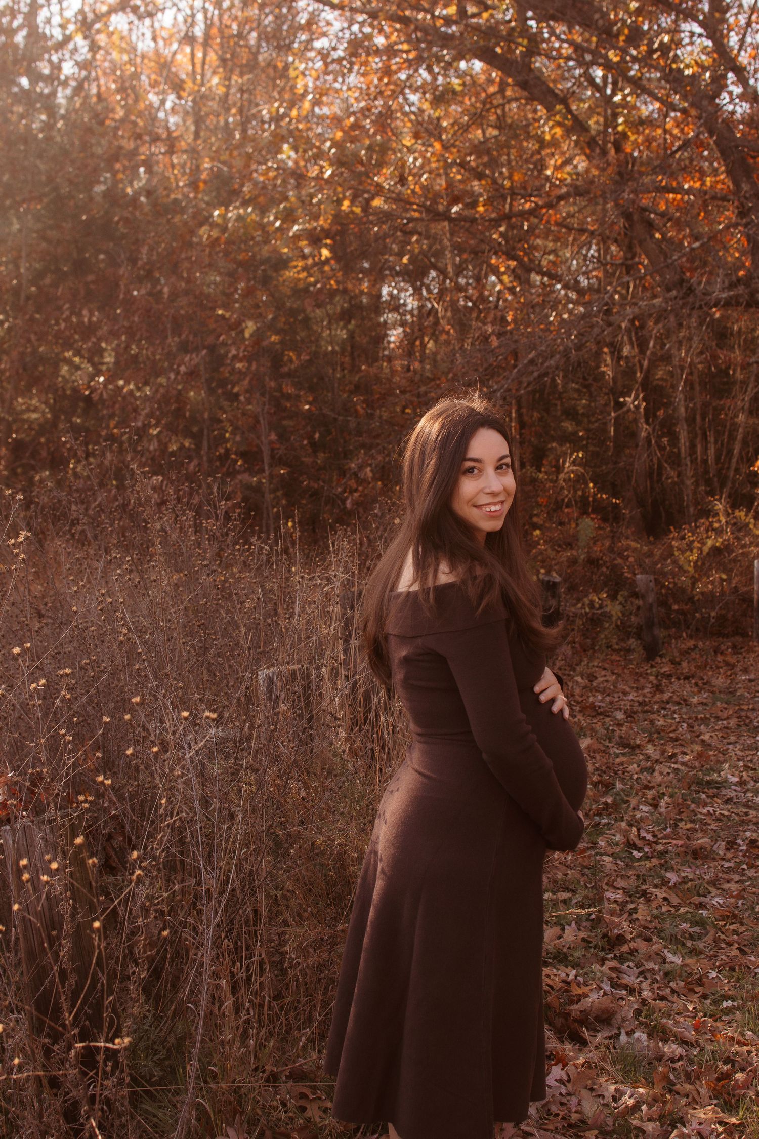 A figure in a brown sweater poses playfully in an autumn forest setting with warm orange foliage.
