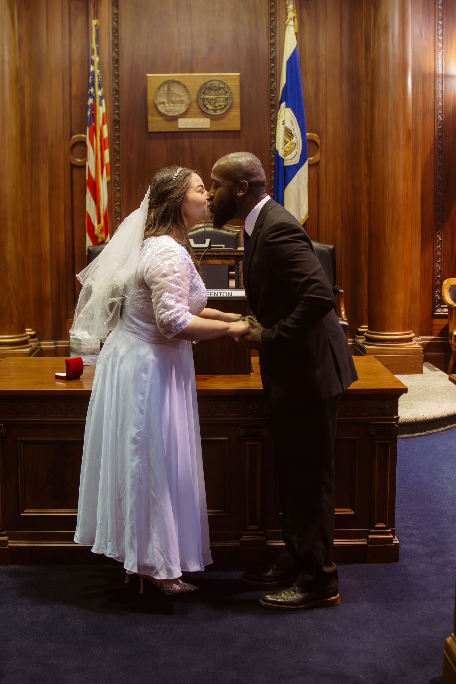 A couple in formal attire shares a kiss during a courthouse wedding ceremony.
