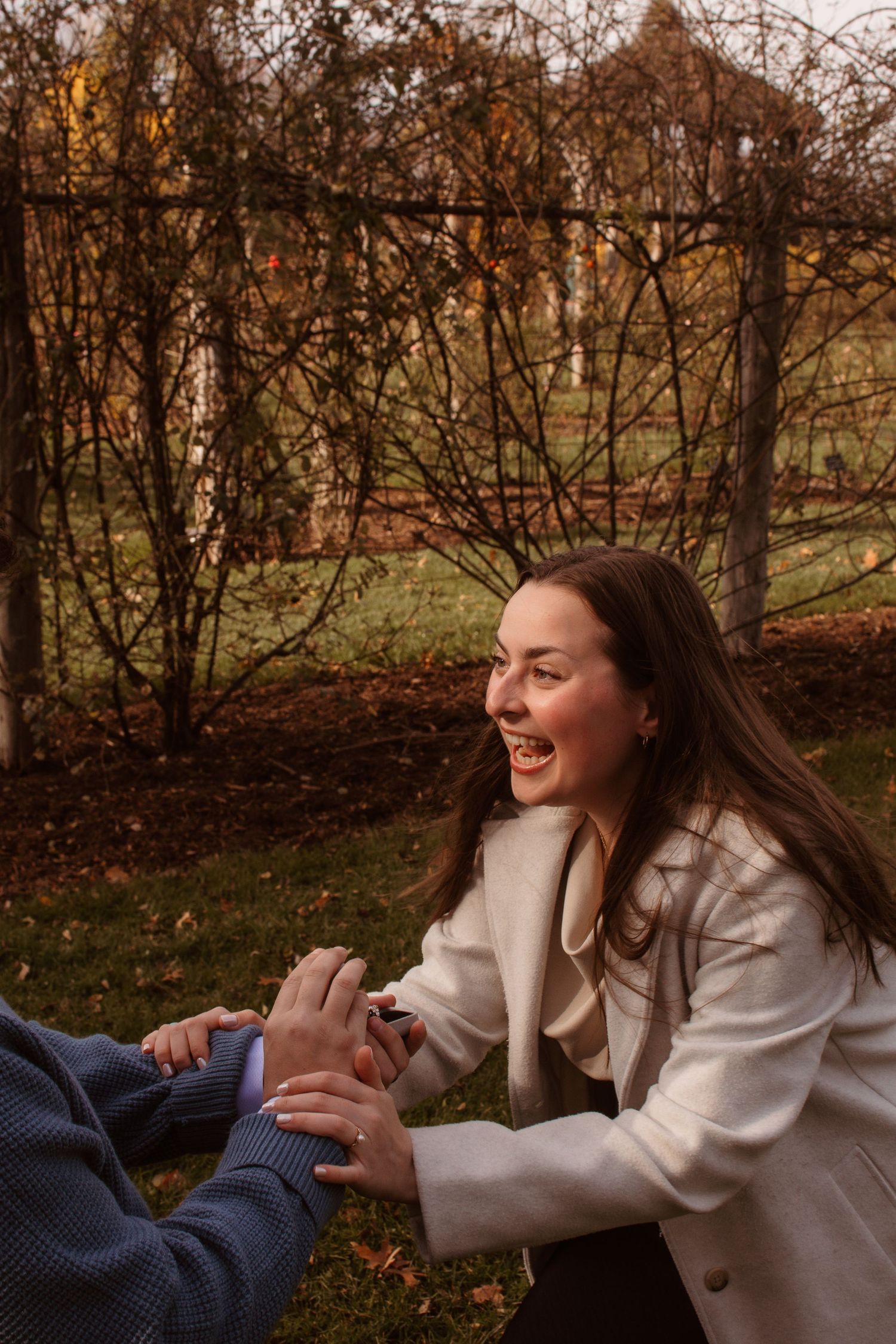 A joyful moment shared between two people sitting on autumn leaves in a park with bare trees in the background.