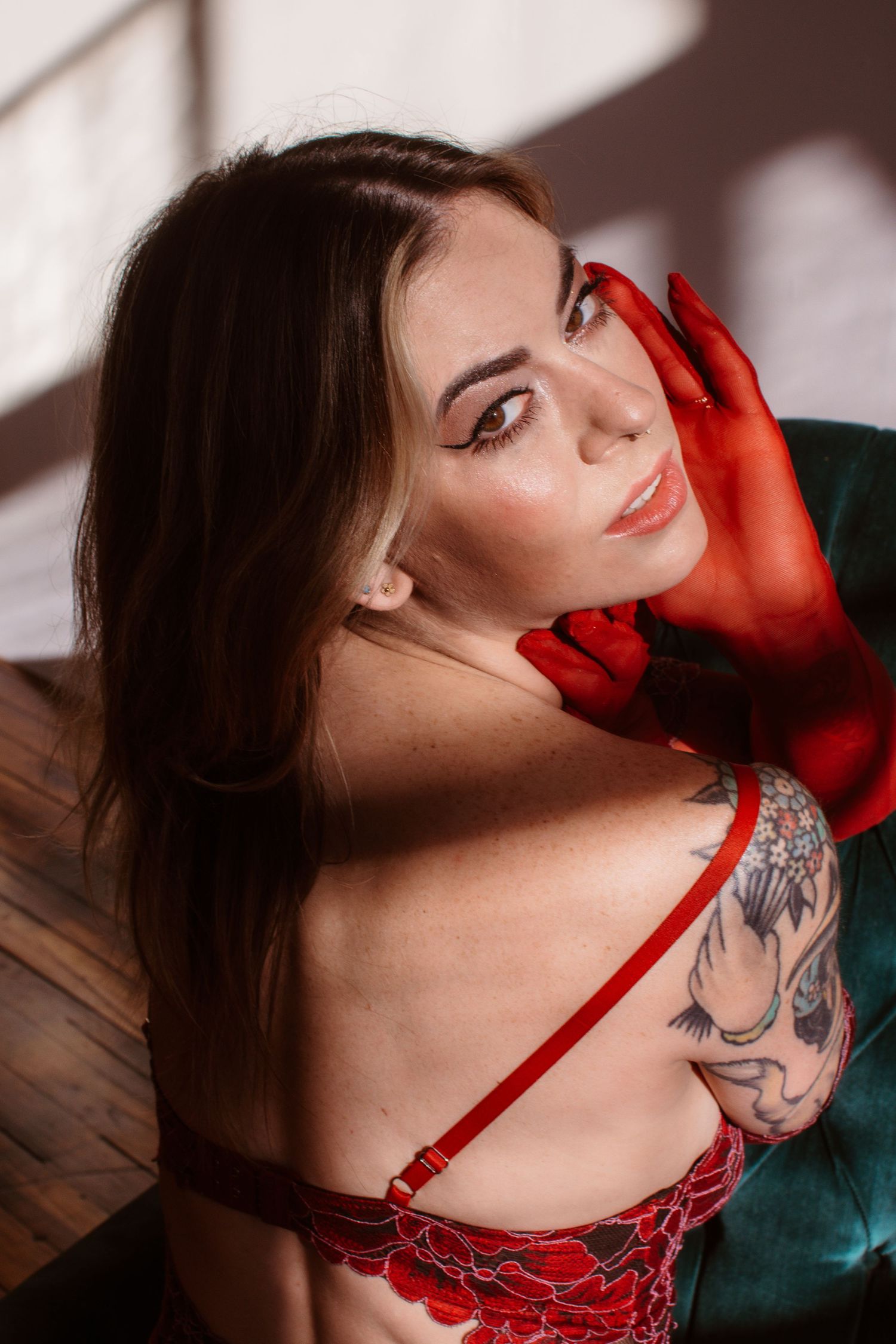A person in red lingerie poses seductively against a dark green velvet couch.
