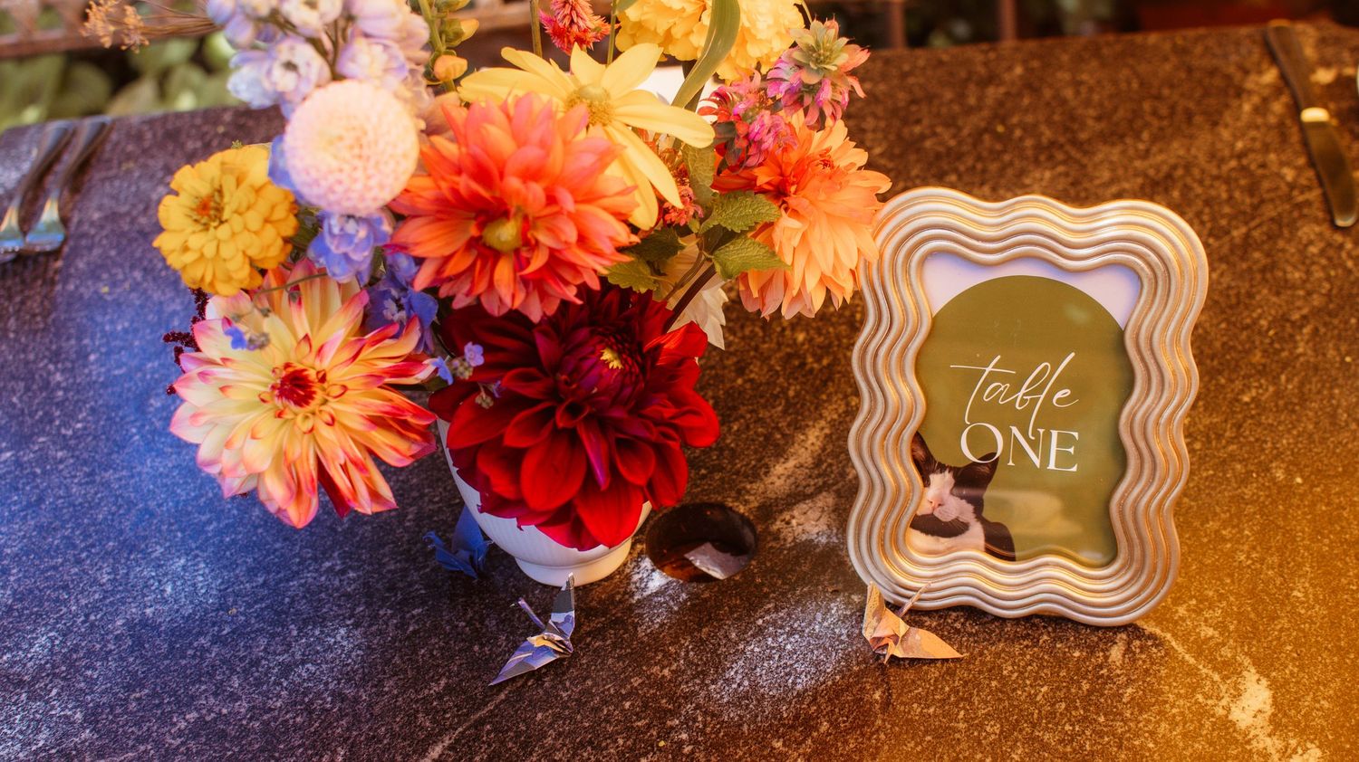 Colorful autumn floral arrangements with dahlias and roses displayed on a dark wooden surface with decorative signs.