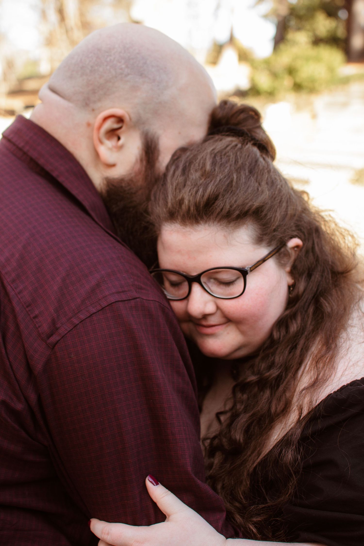 Intimate romantic portrait of a couple embracing outdoors, with one person wearing glasses and a dark coat.