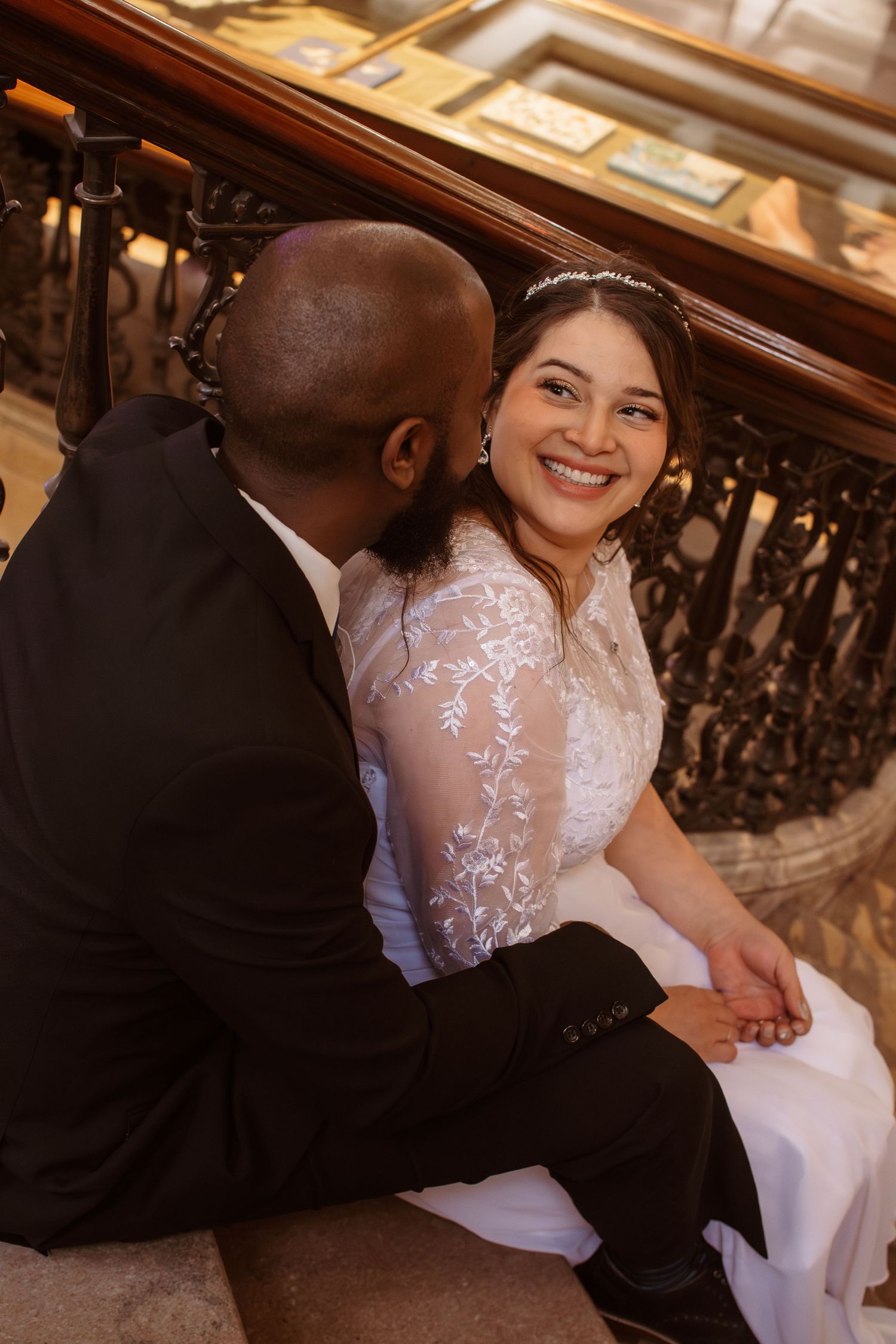 Newlyweds share tender moments on ornate staircase during their wedding photoshoot.
