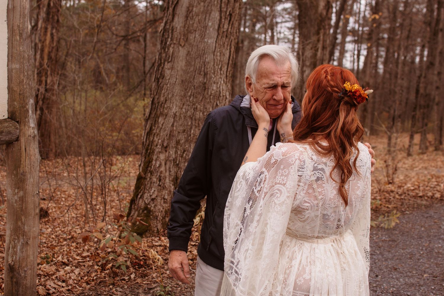 A couple walks together on a wooded path surrounded by autumn foliage and fallen leaves.