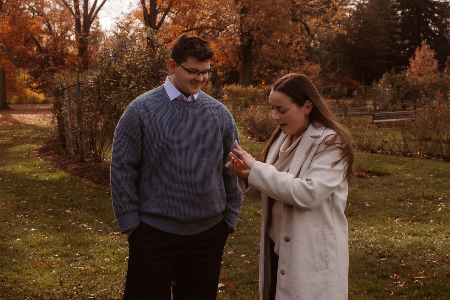 Couple walking together in a scenic autumn park with orange and brown fall foliage in the background.