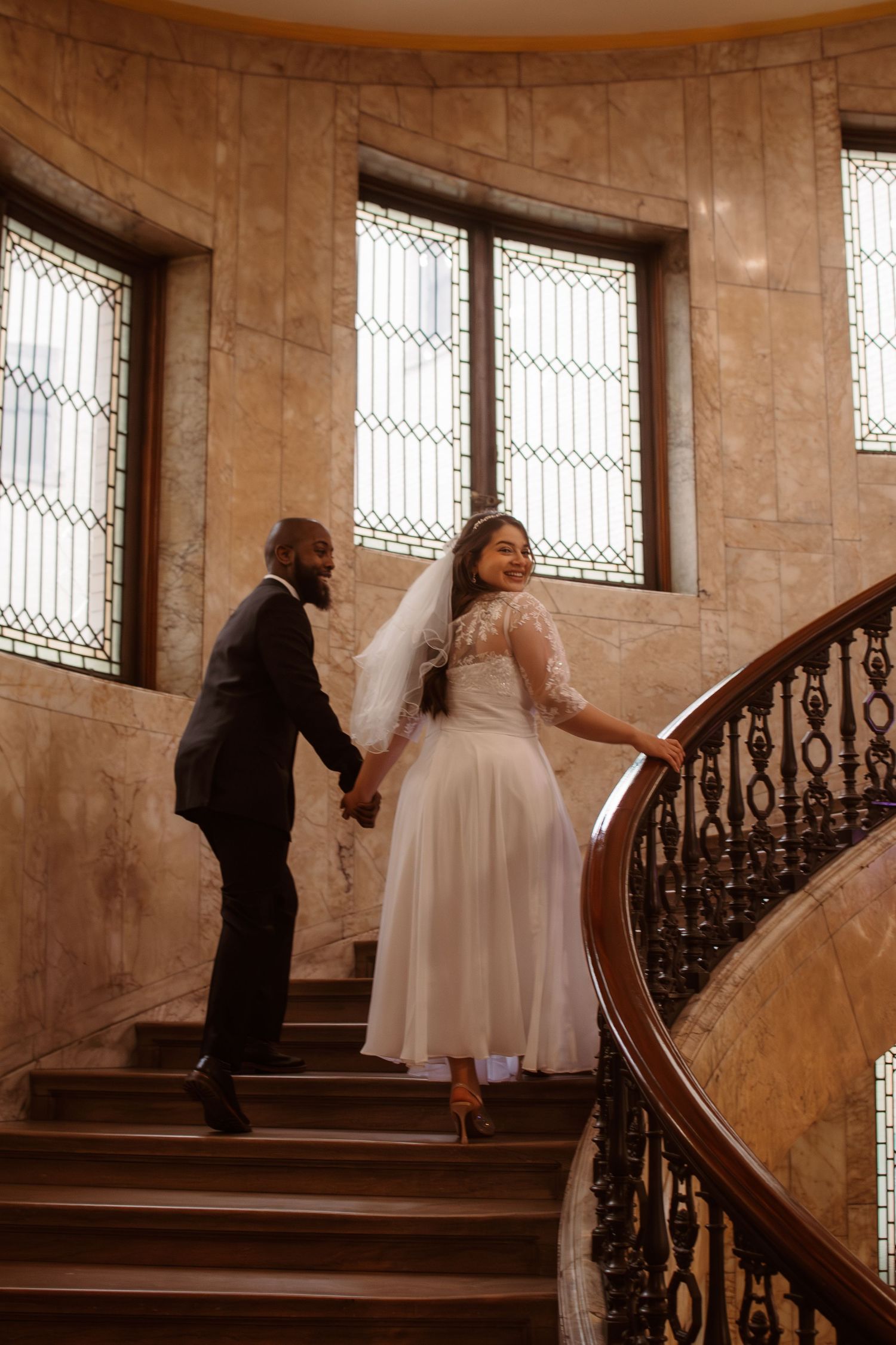 A series of photos showing a couple in wedding attire ascending a grand staircase with ornate railings in a stone building.