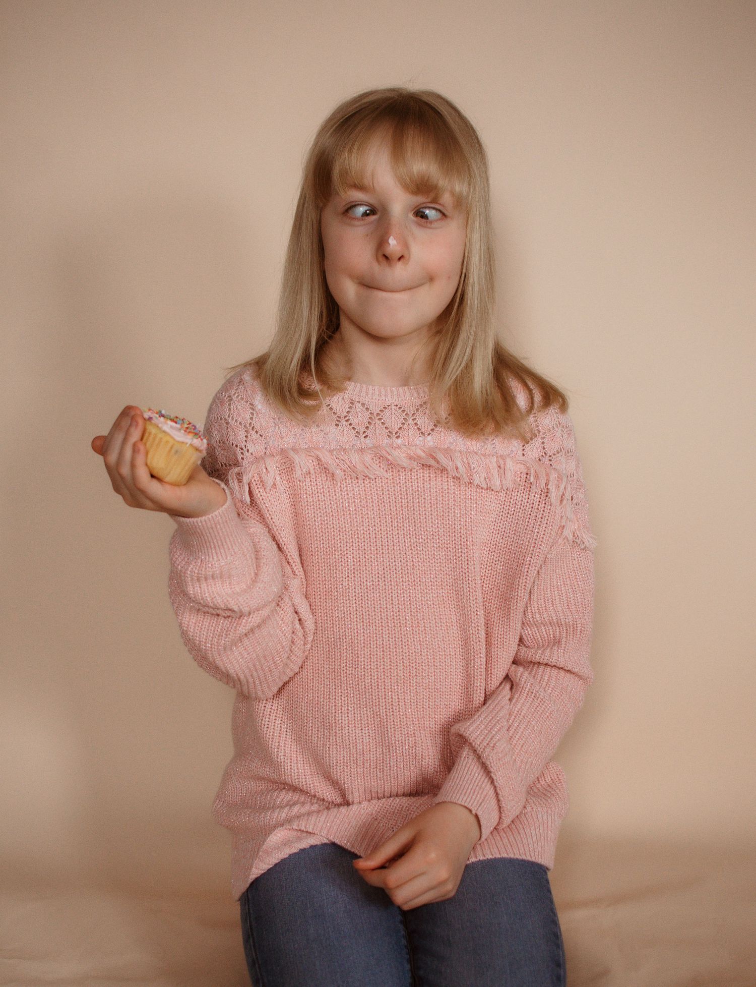 Person in pink knit sweater with lace detail holds a cookie while sitting against neutral background.