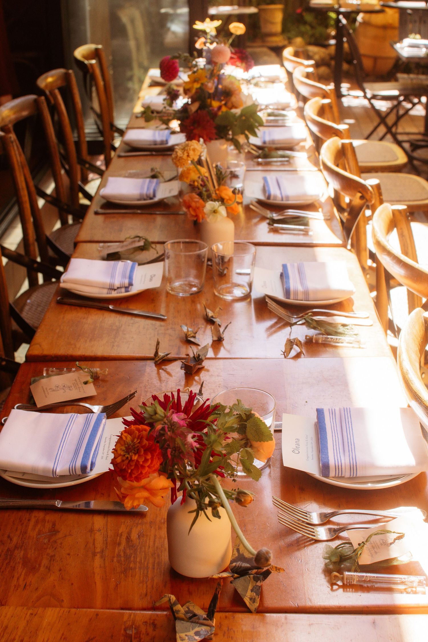 Elegant table setting with wooden chairs and white place settings adorned with autumn floral centerpieces in warm lighting.