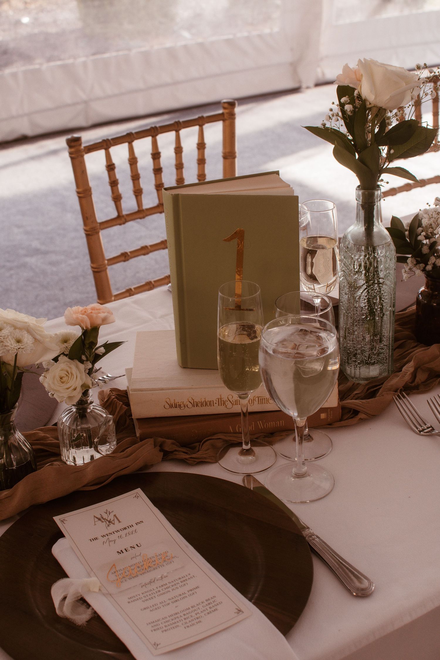 Elegant wedding table setting with champagne glasses, floral centerpiece, green book table number, and personalized menu card.