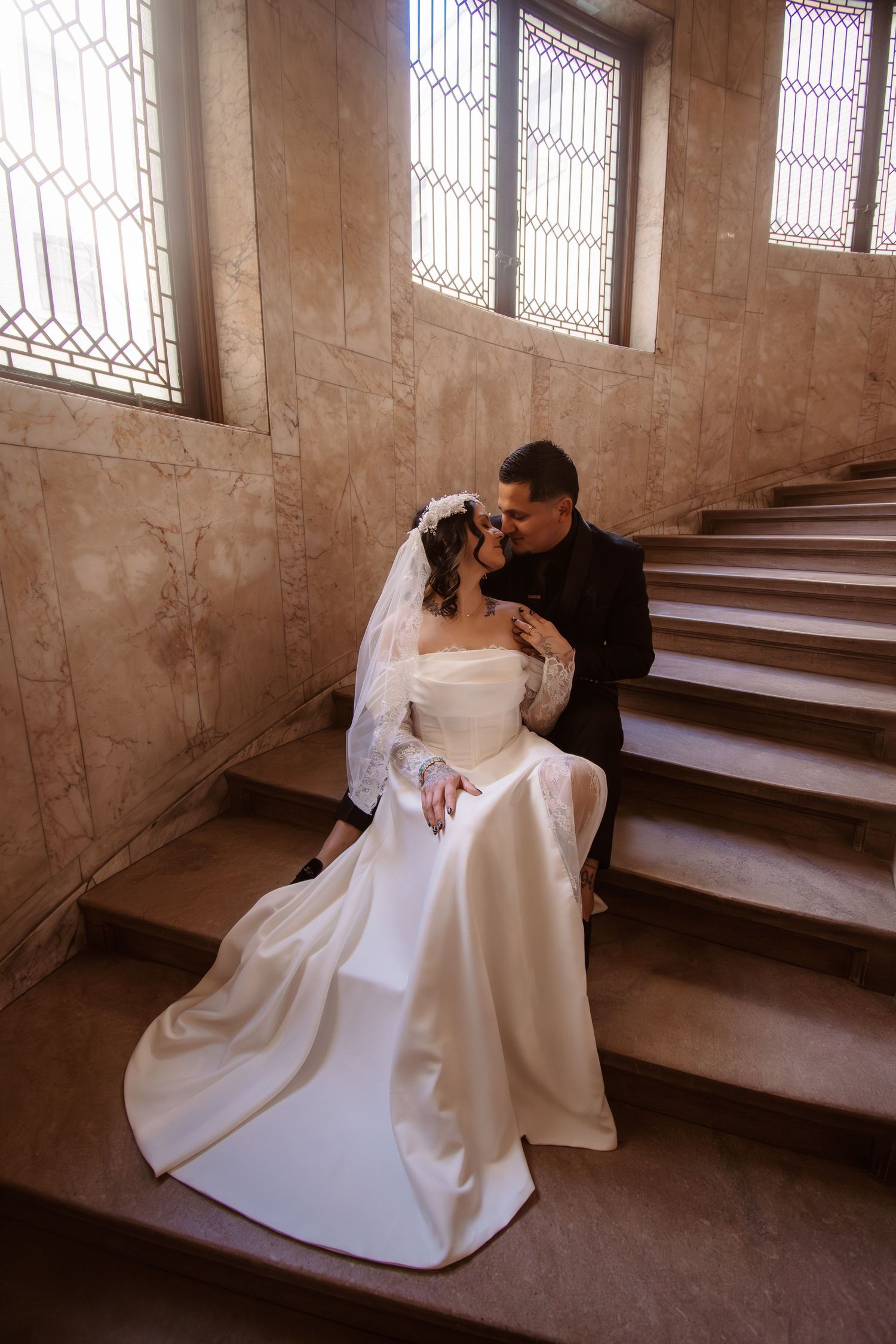 Bride and groom share a romantic moment on ornate marble staircase, bride in elegant white gown with veil.