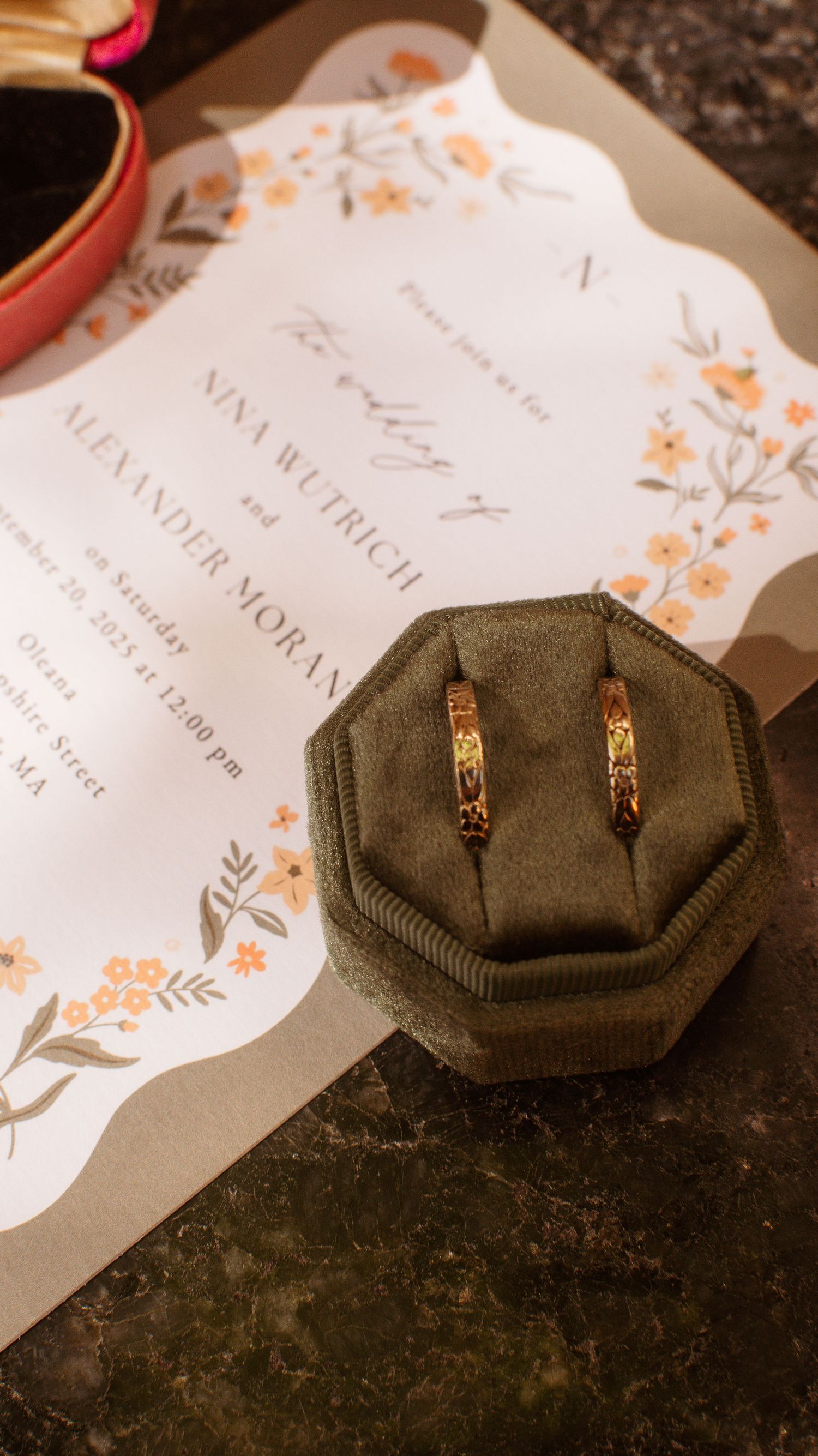 Wedding name cards and gold earrings displayed on a dark surface with delicate floral designs.