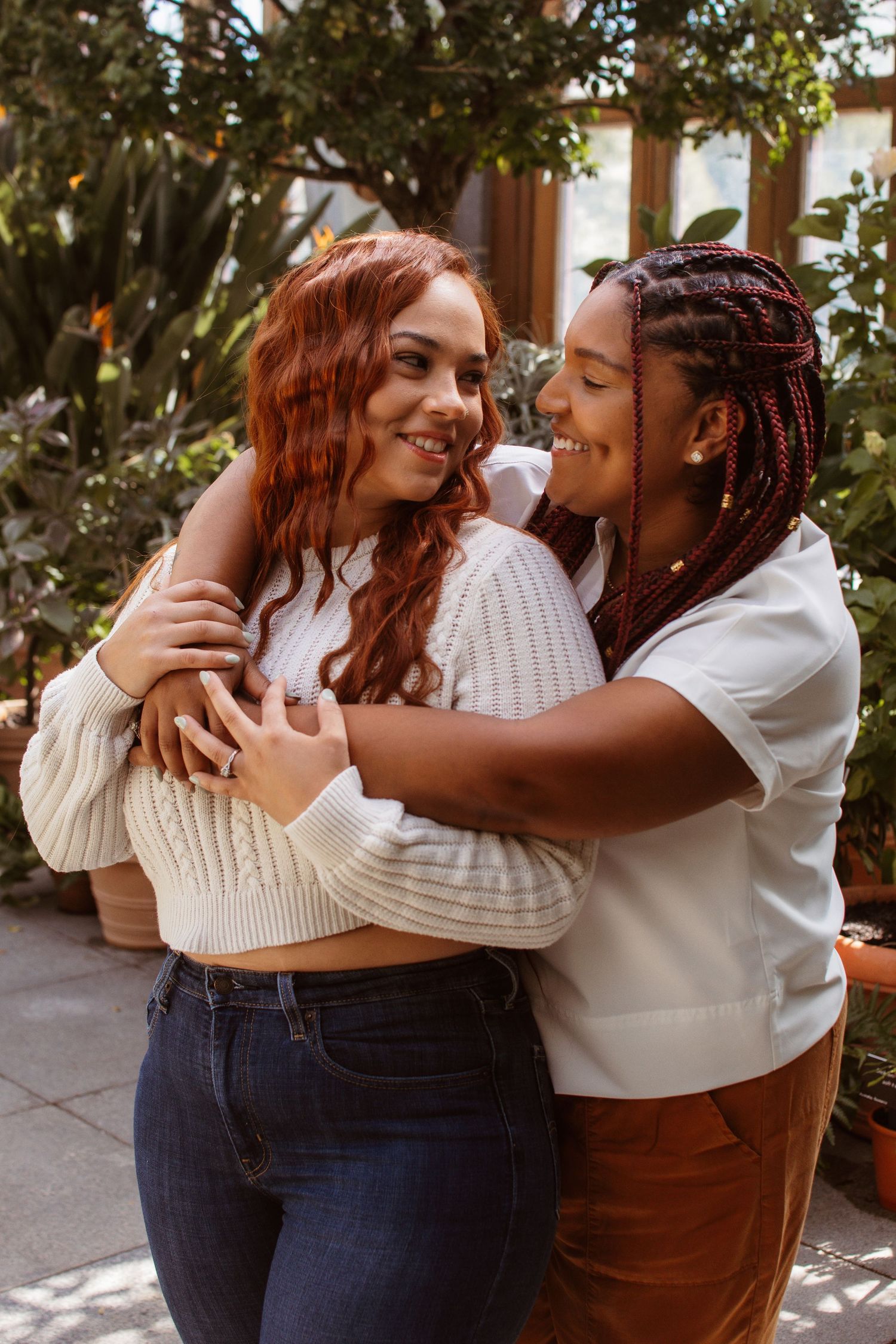 Two people sharing an intimate embrace and laughing together in a sunny outdoor setting with greenery in the background.