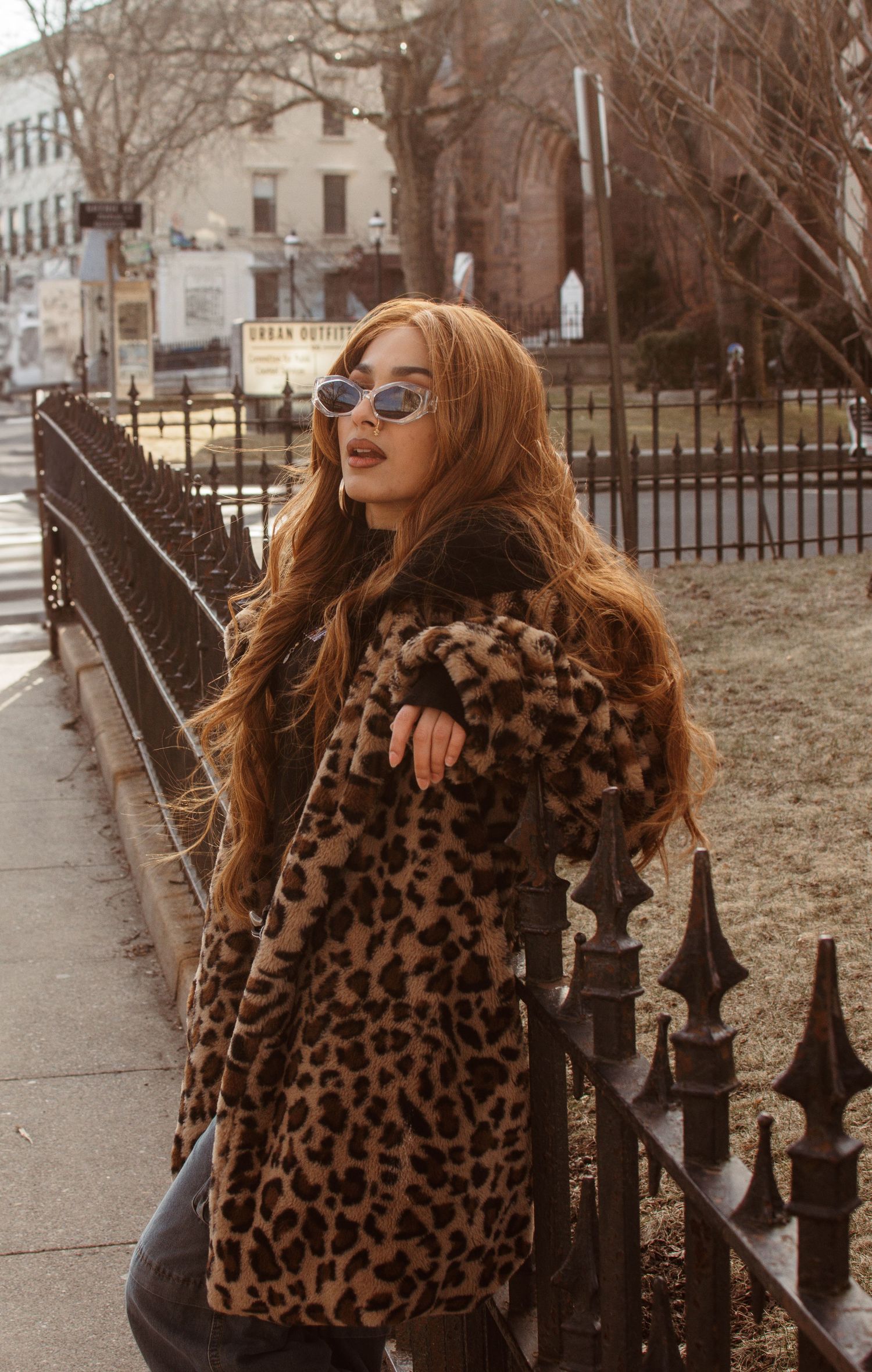 Winter street fashion featuring leopard print faux fur coat, sunglasses and long hair in muted urban setting.