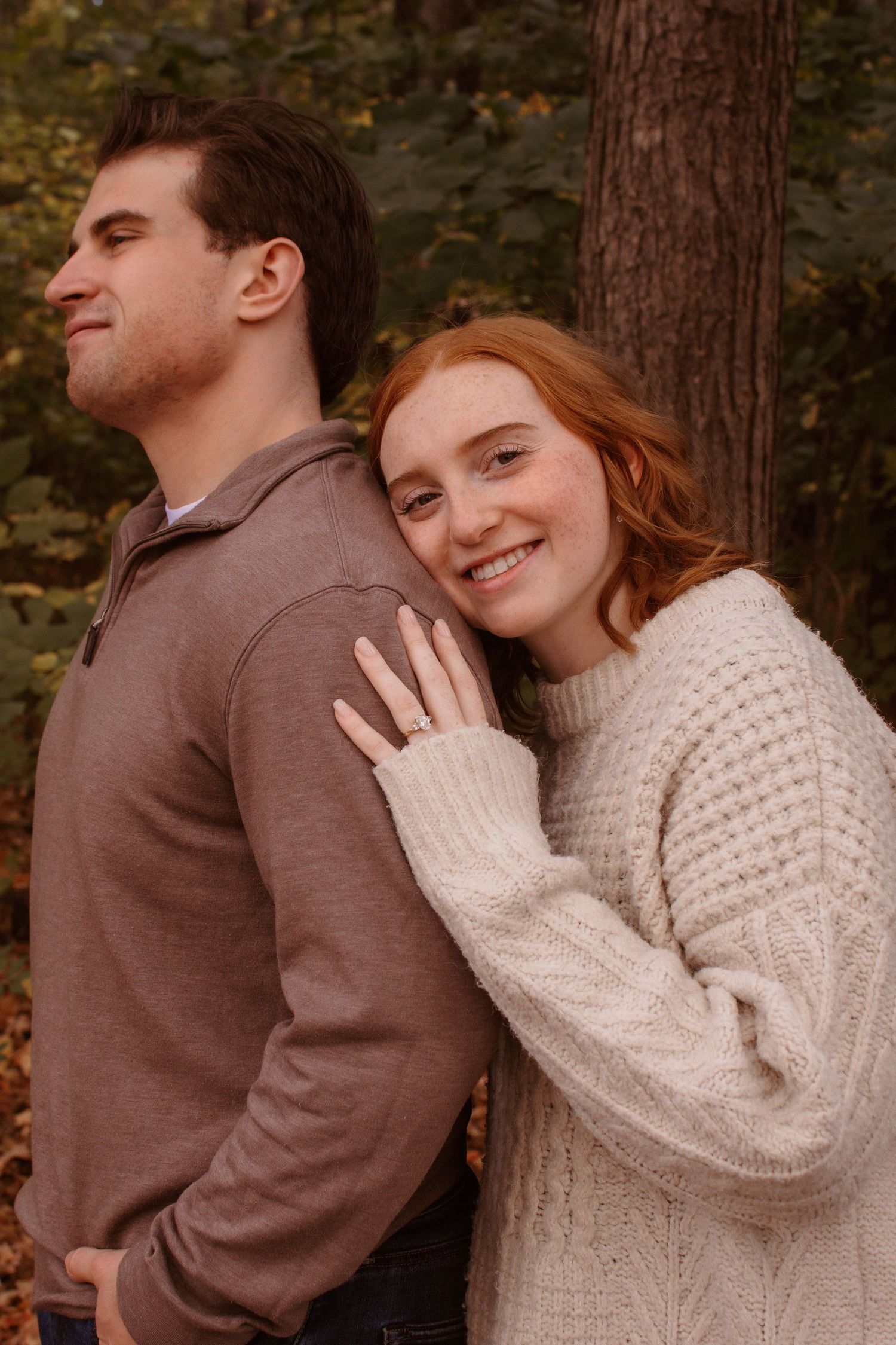 A couple in cozy sweaters shares intimate moments in a romantic autumn forest photoshoot.