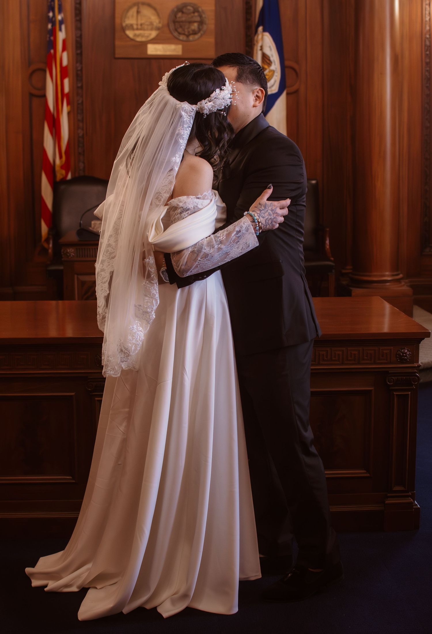 Bride and groom share first kiss in elegant courthouse wedding ceremony, bride wearing white gown and veil.