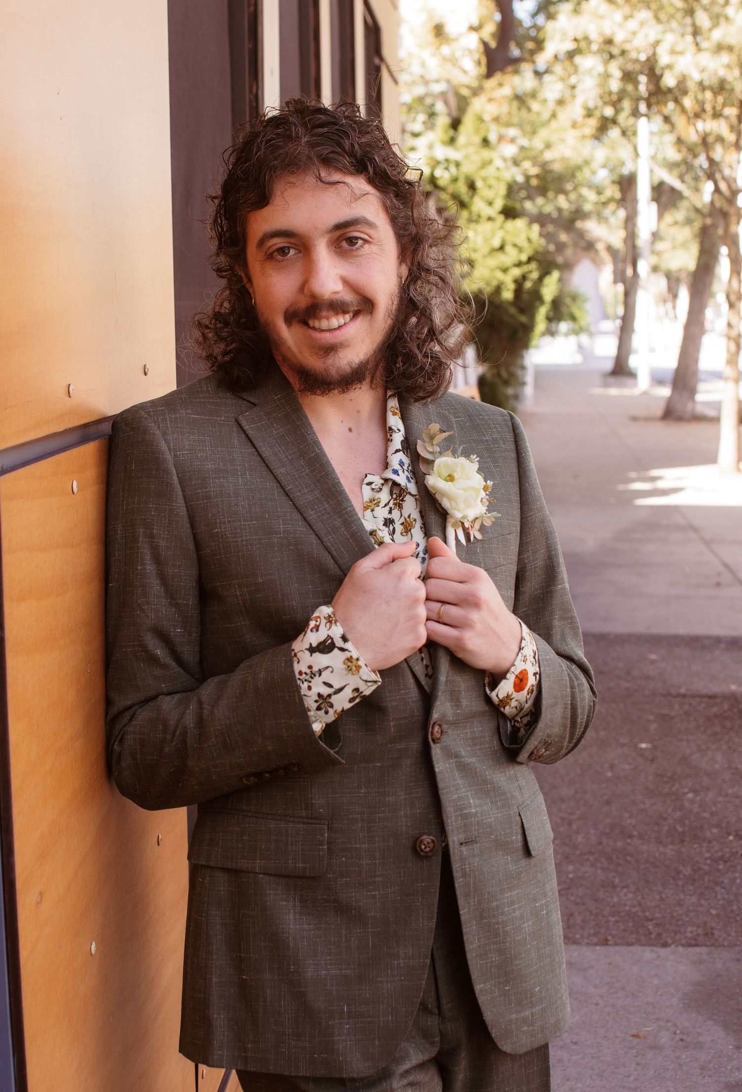 A person in a dark suit jacket stands against a wall in warm outdoor lighting.