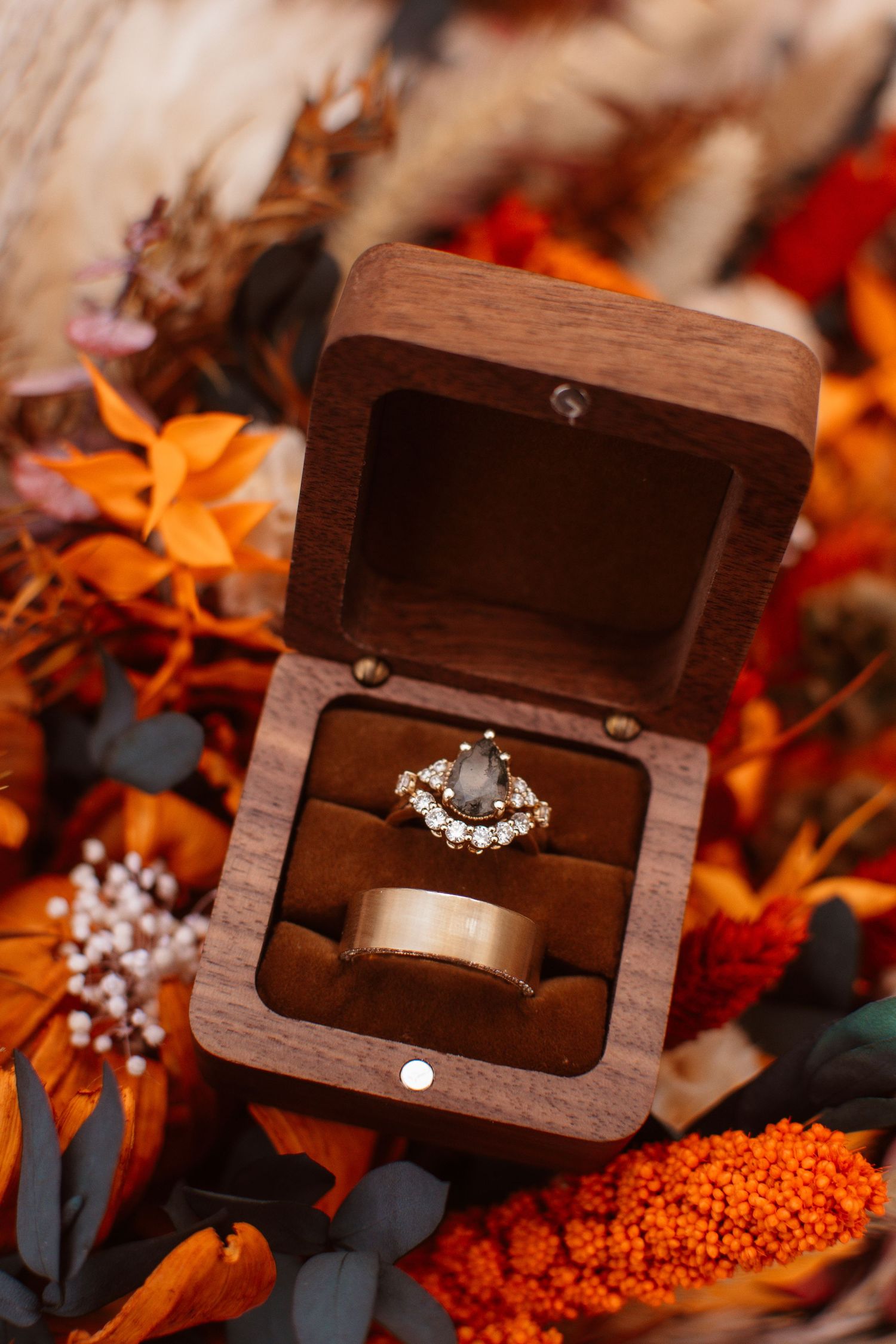 Diamond engagement ring in wooden box surrounded by orange autumn leaves and berries creates romantic scene.