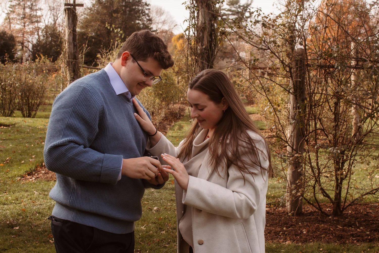 A couple shares romantic moments in a fall setting with autumn foliage and trees in the background.