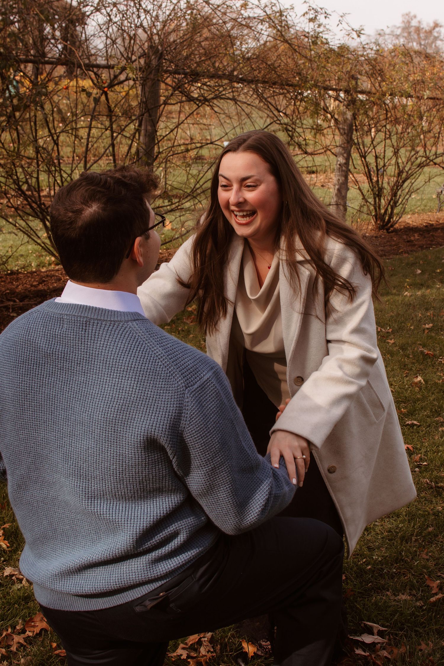 A candid moment of laughter between two people sitting outdoors on fallen leaves during autumn.